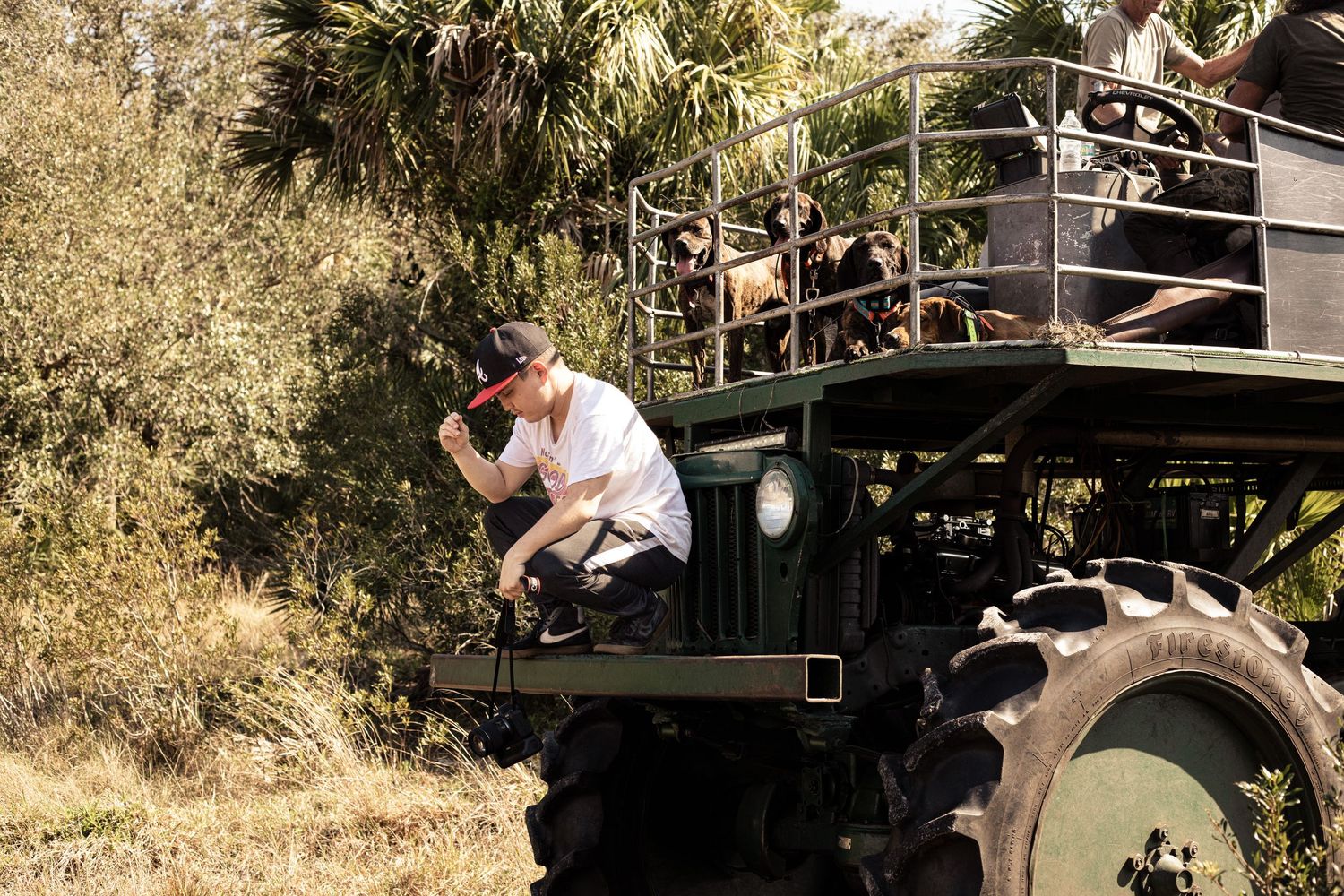 Man climbing onto a large green military truck on a safari tour with passengers in the elevated viewing platform.