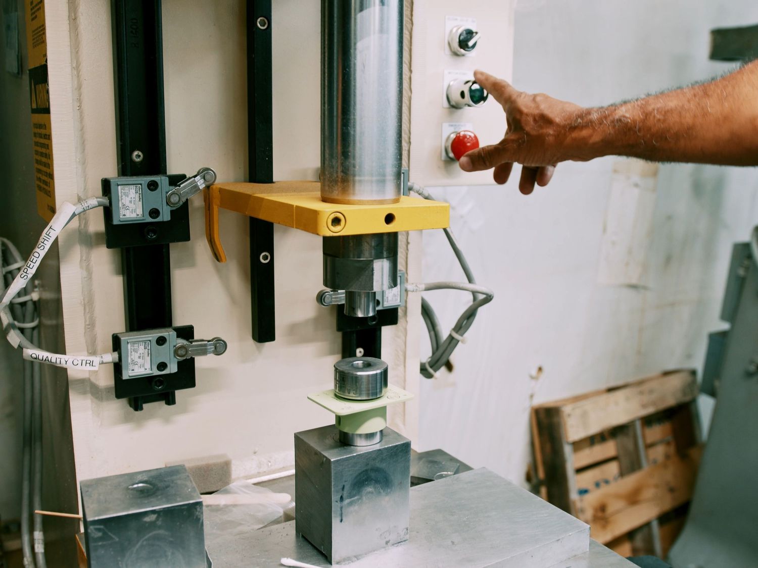 Worker operates industrial press machine with yellow frame and control panel in manufacturing facility.