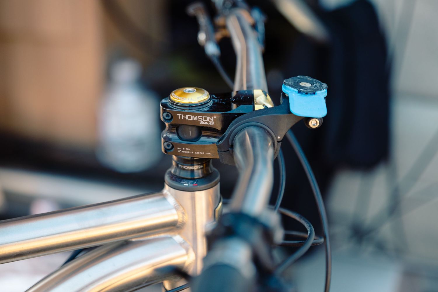 Close-up of a Thomson bike stem with a blue bell mounted on a titanium bicycle handlebar.