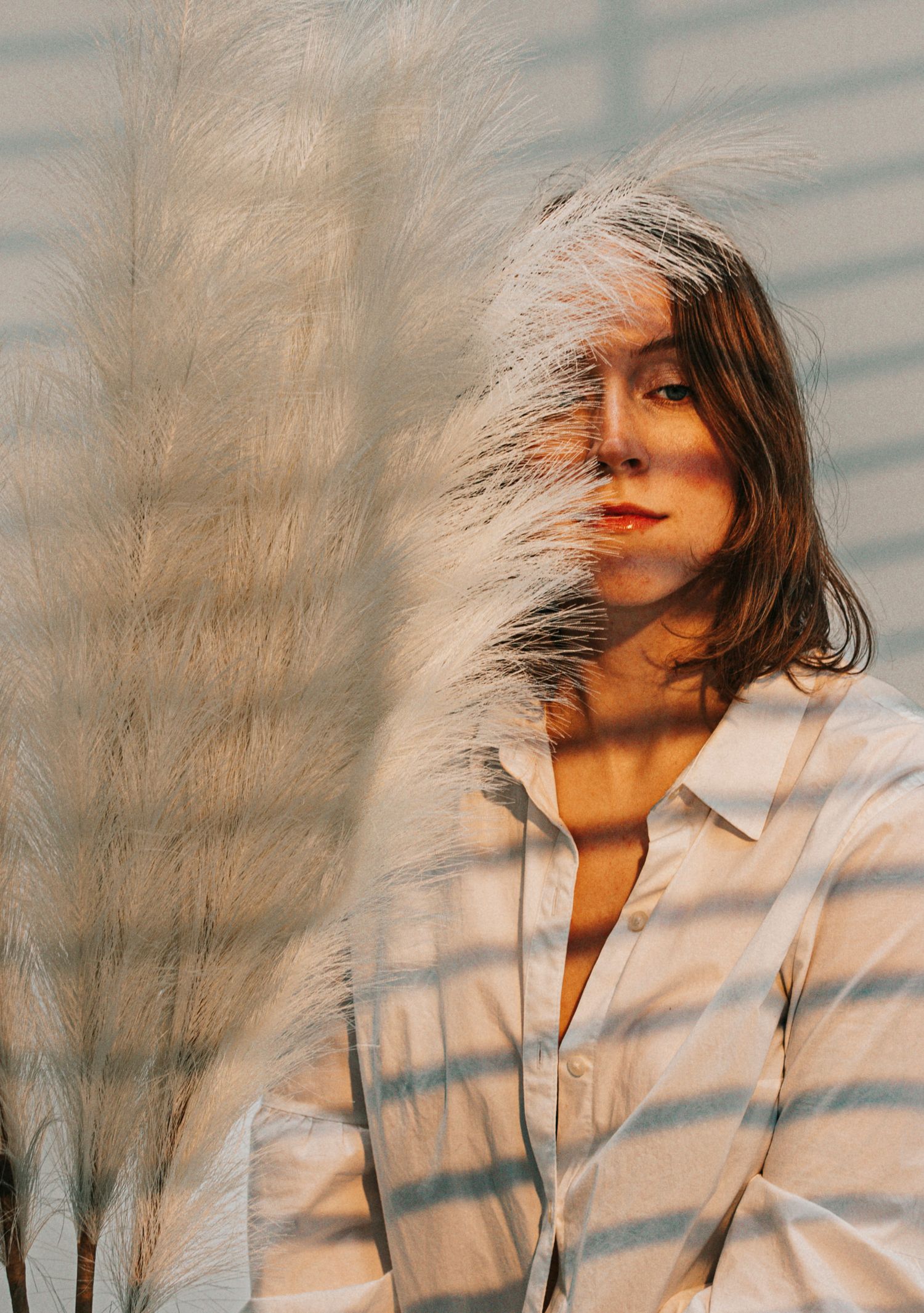 Woman in striped shirt partially obscured by white pampas grass in warm sunlight.