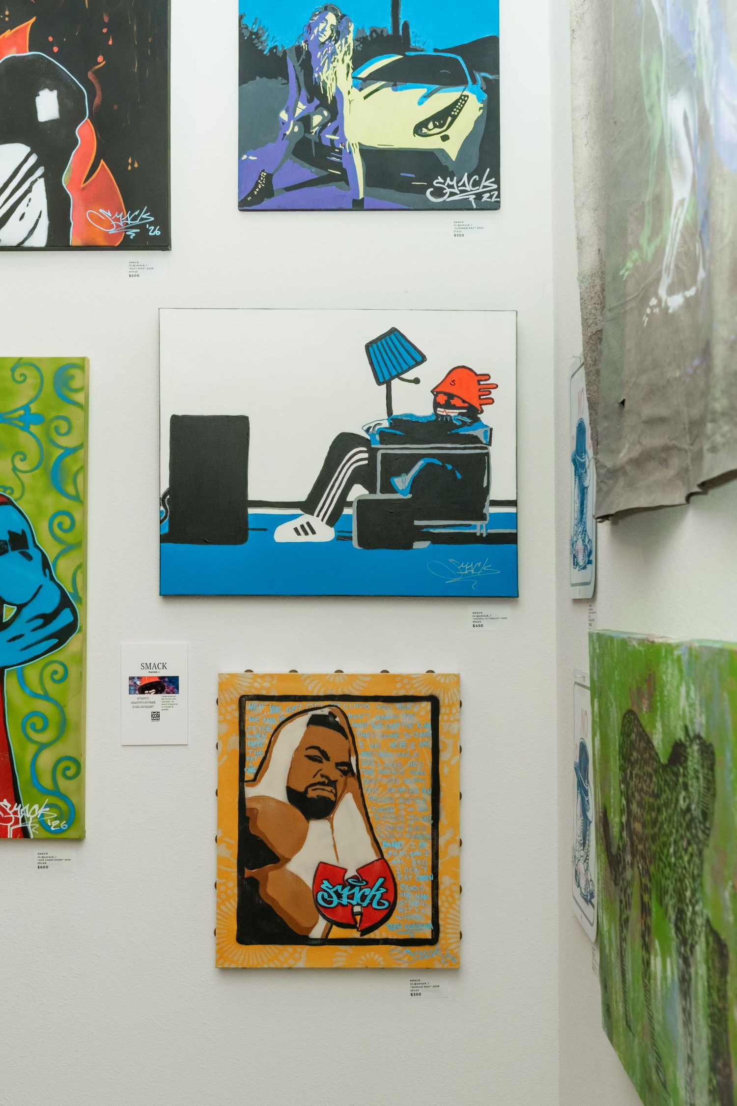 Bold pop art paintings including street art portraits displayed on white gallery wall.