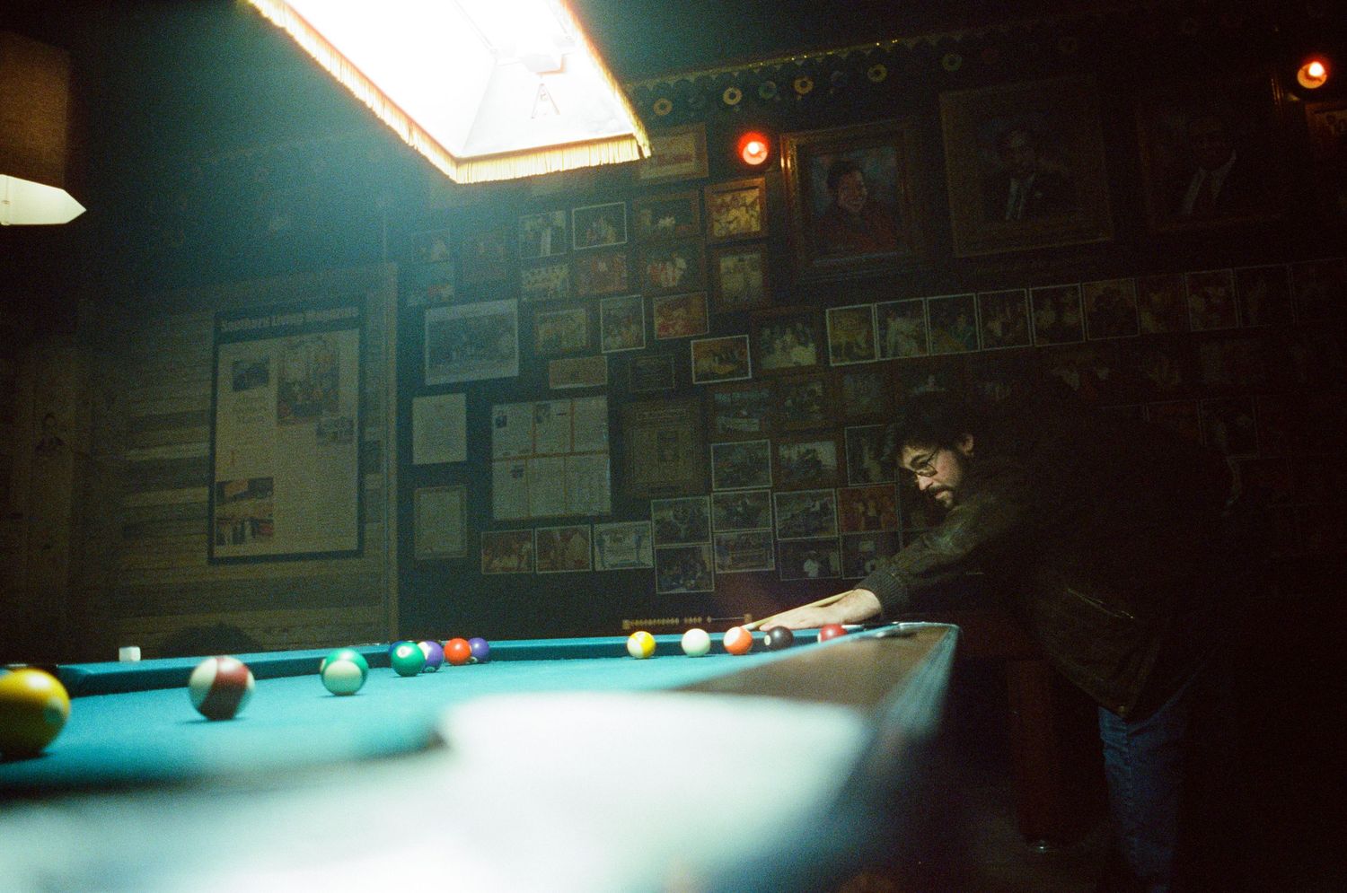 Person playing pool in a dimly lit bar with colorful billiard balls on a green felt table.