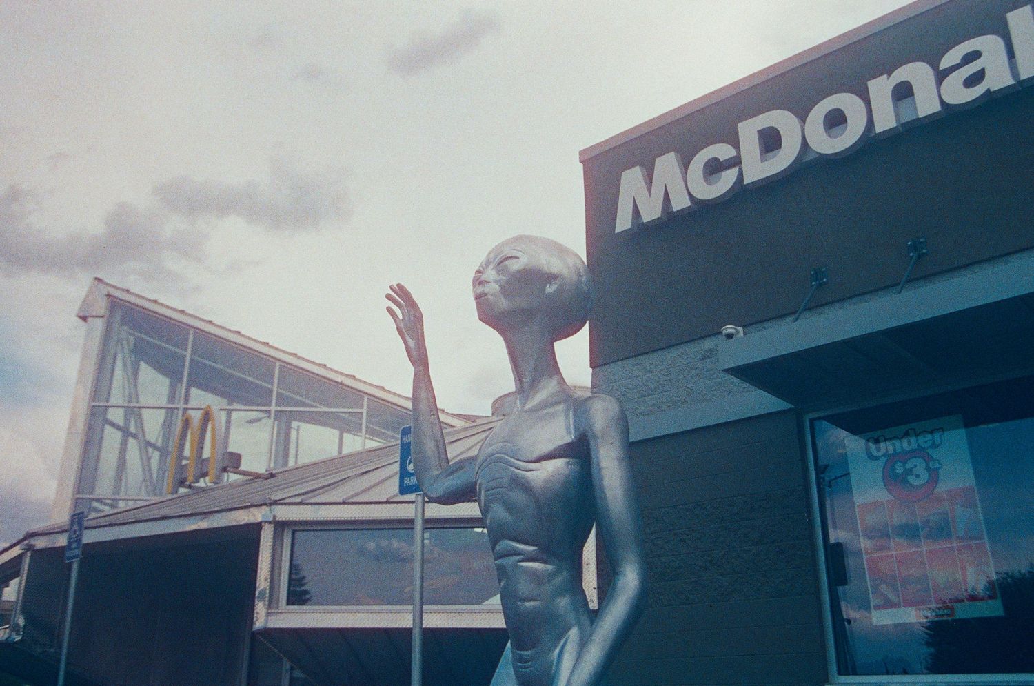 Alien statue posing in front of a McDonald's restaurant under a cloudy sky.