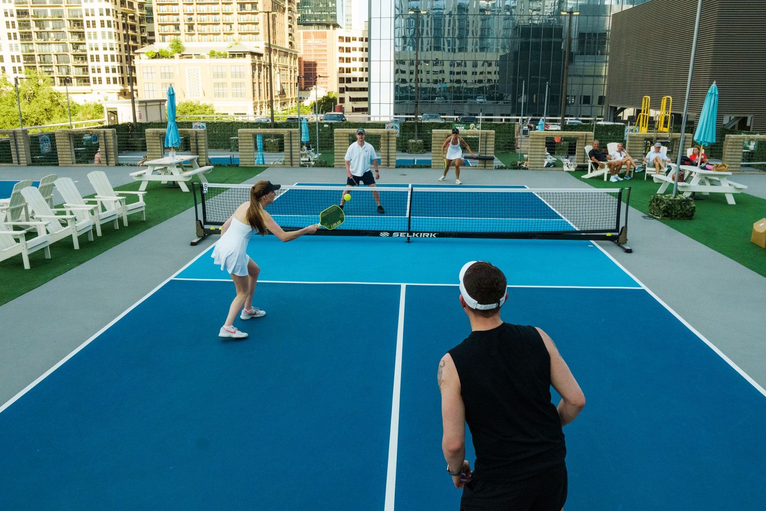 Players compete on a rooftop pickleball court with city skyline views on a sunny day.