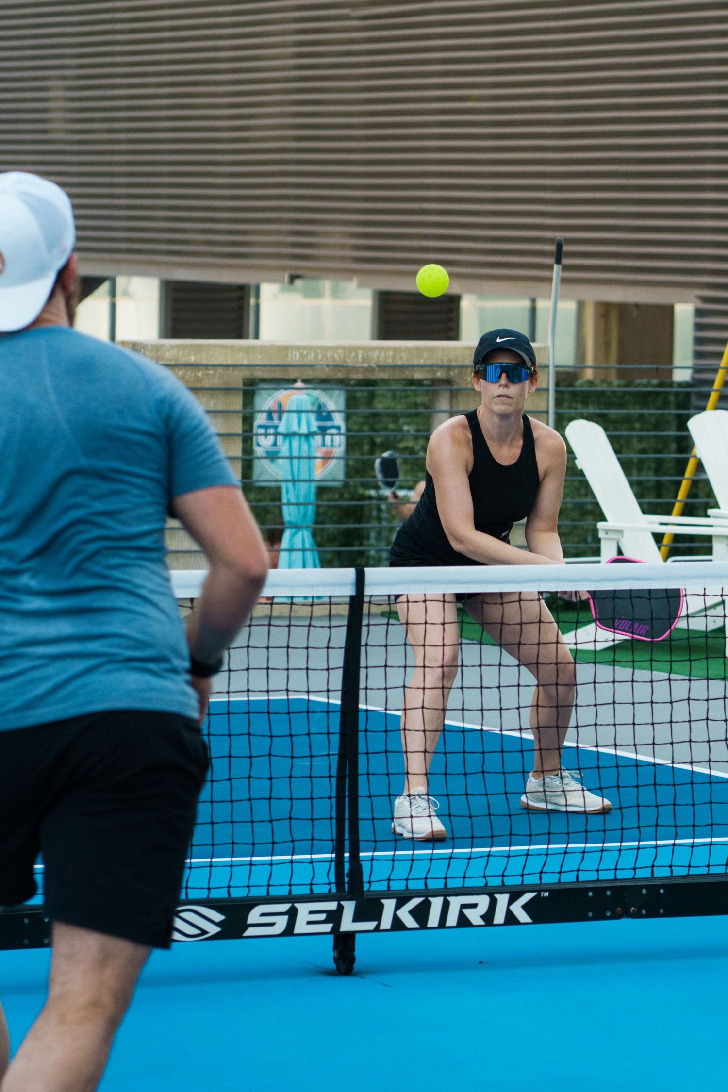 Two players compete in a pickleball match on a Selkirk court, with a woman in black ready at the net.