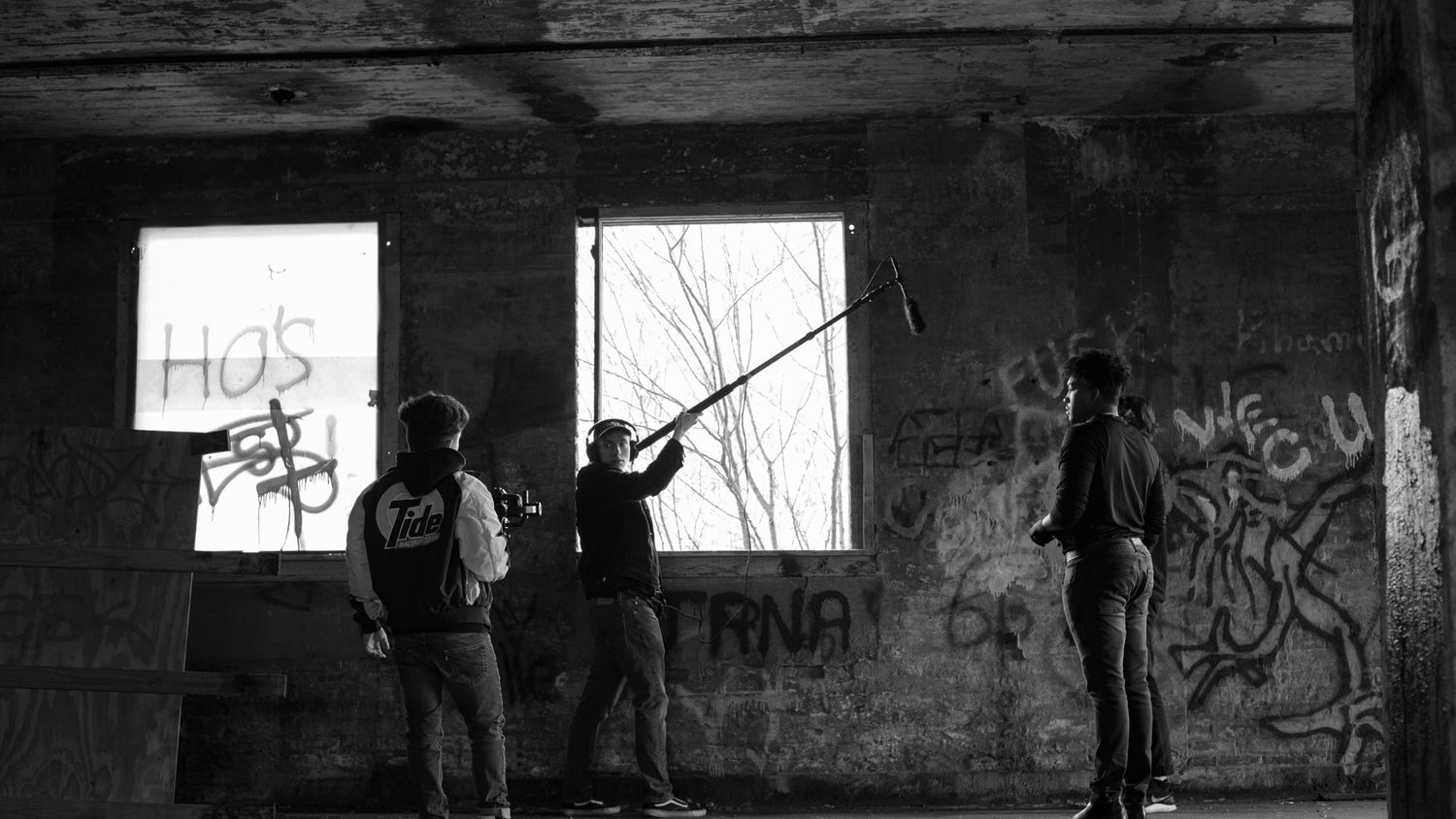Black and white photo of three people filming in an abandoned graffiti-covered building with a boom mic.