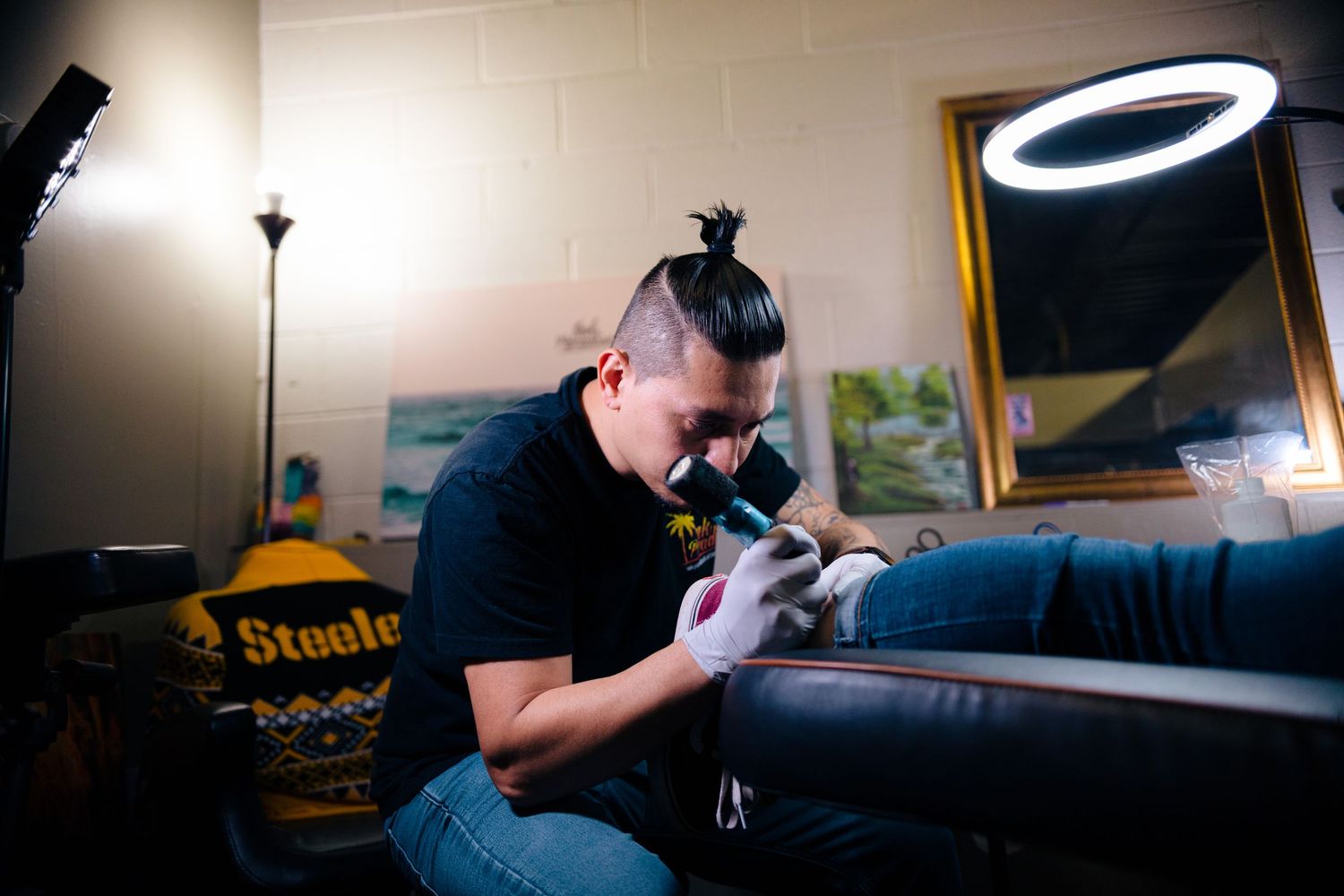 Tattoo artist carefully inking a client's arm under a ring light in a professional tattoo studio.