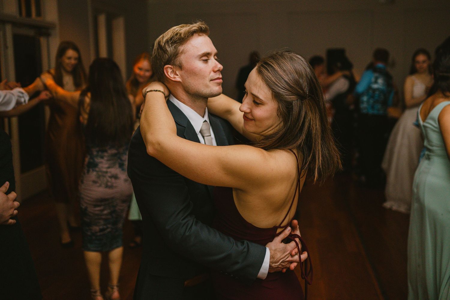 Couple sharing an intimate slow dance embrace at a lively indoor wedding reception celebration.