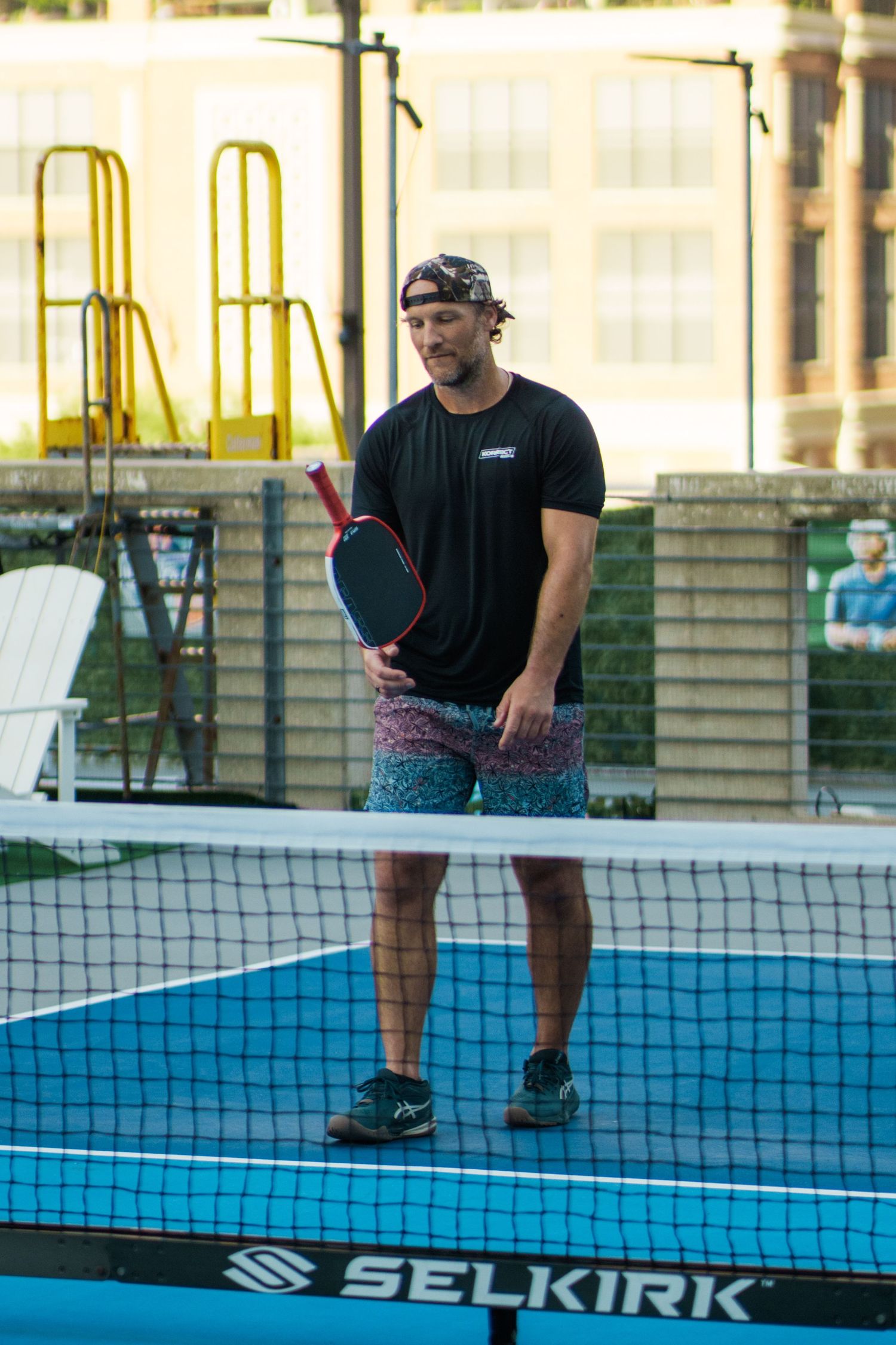 Man in black shirt holding a red pickleball paddle on a Selkirk court outdoors.