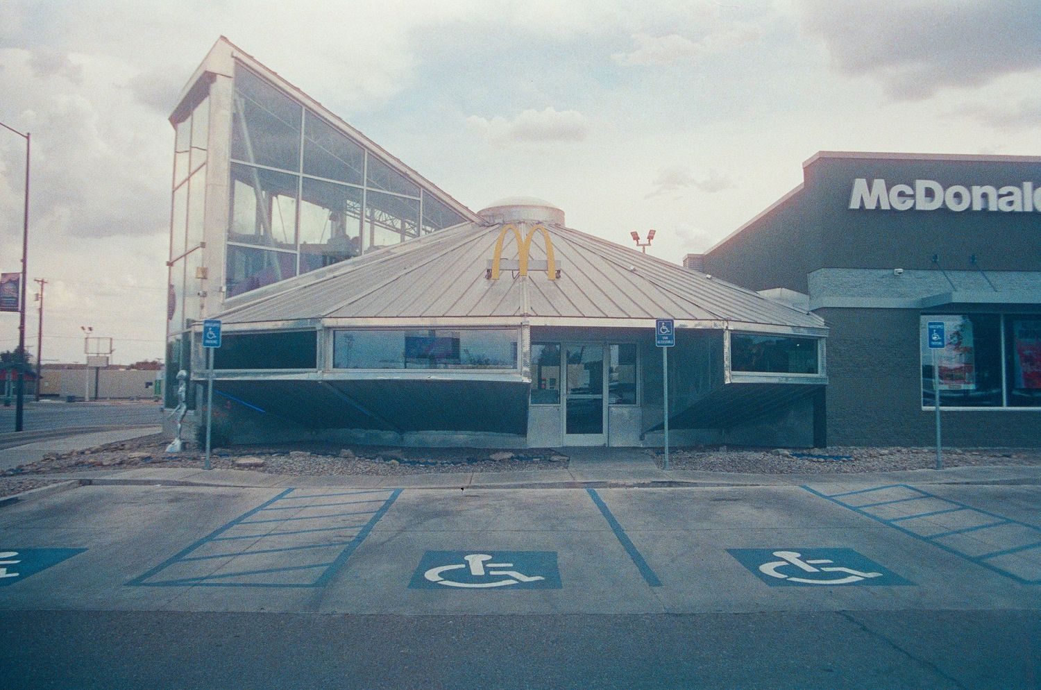 Abandoned circular McDonald's restaurant with handicap parking spaces in an empty lot under overcast skies.