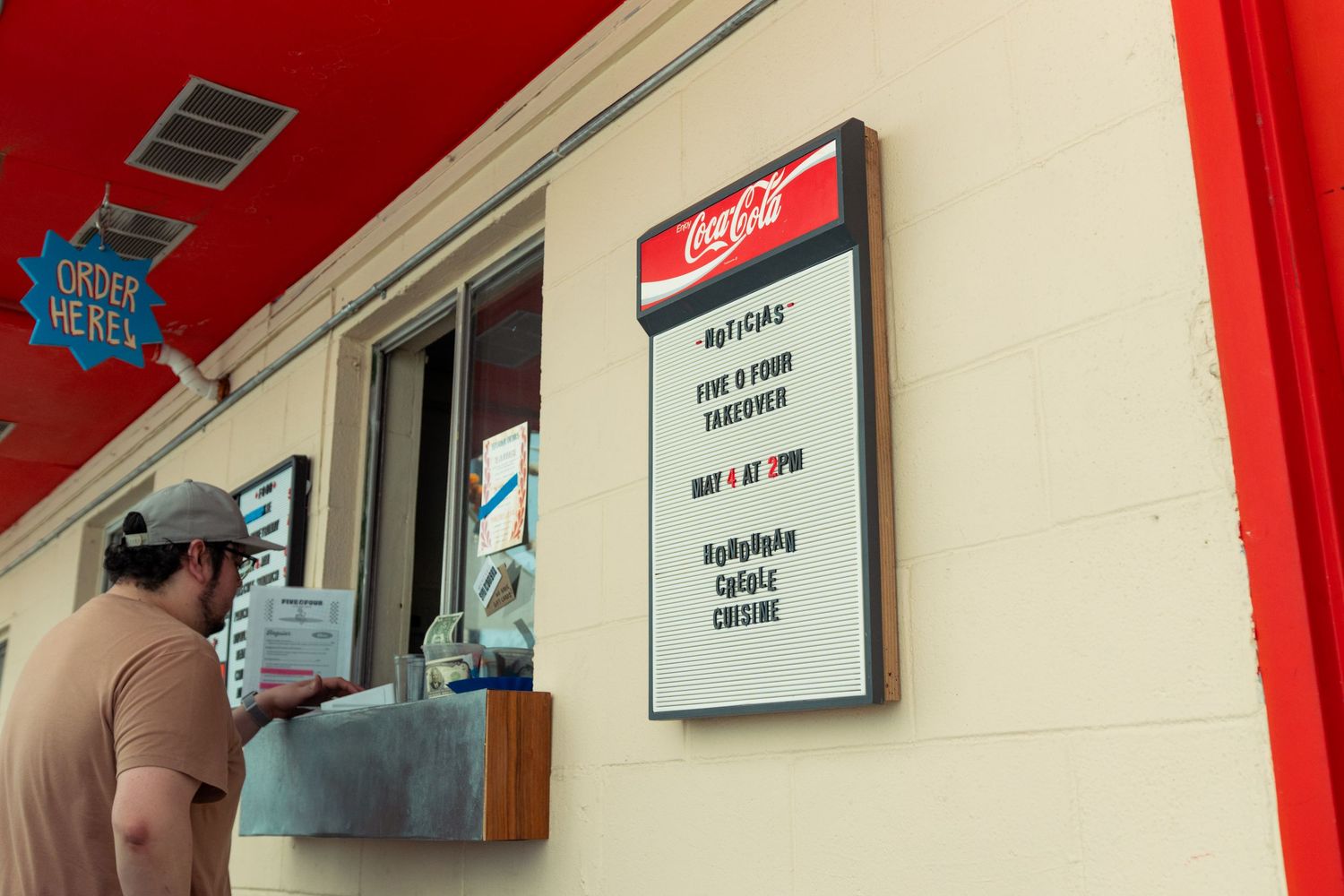 Man reads a Coca-Cola menu board mounted outside a red and white food stand.