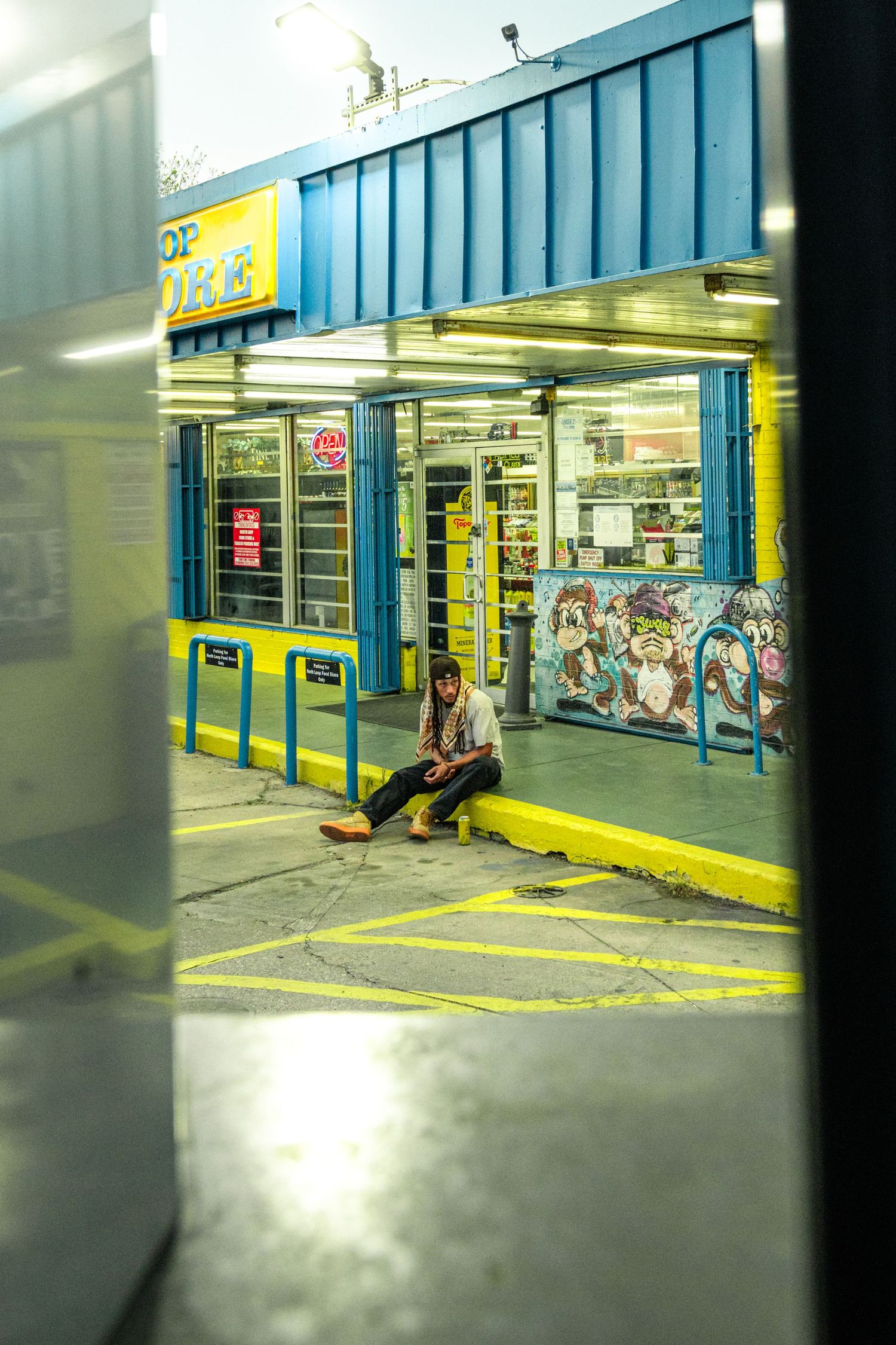 Candid street-style portrait of a man in streetwear outside a vintage blue-and-yellow convenience store, Austin urban photography.
