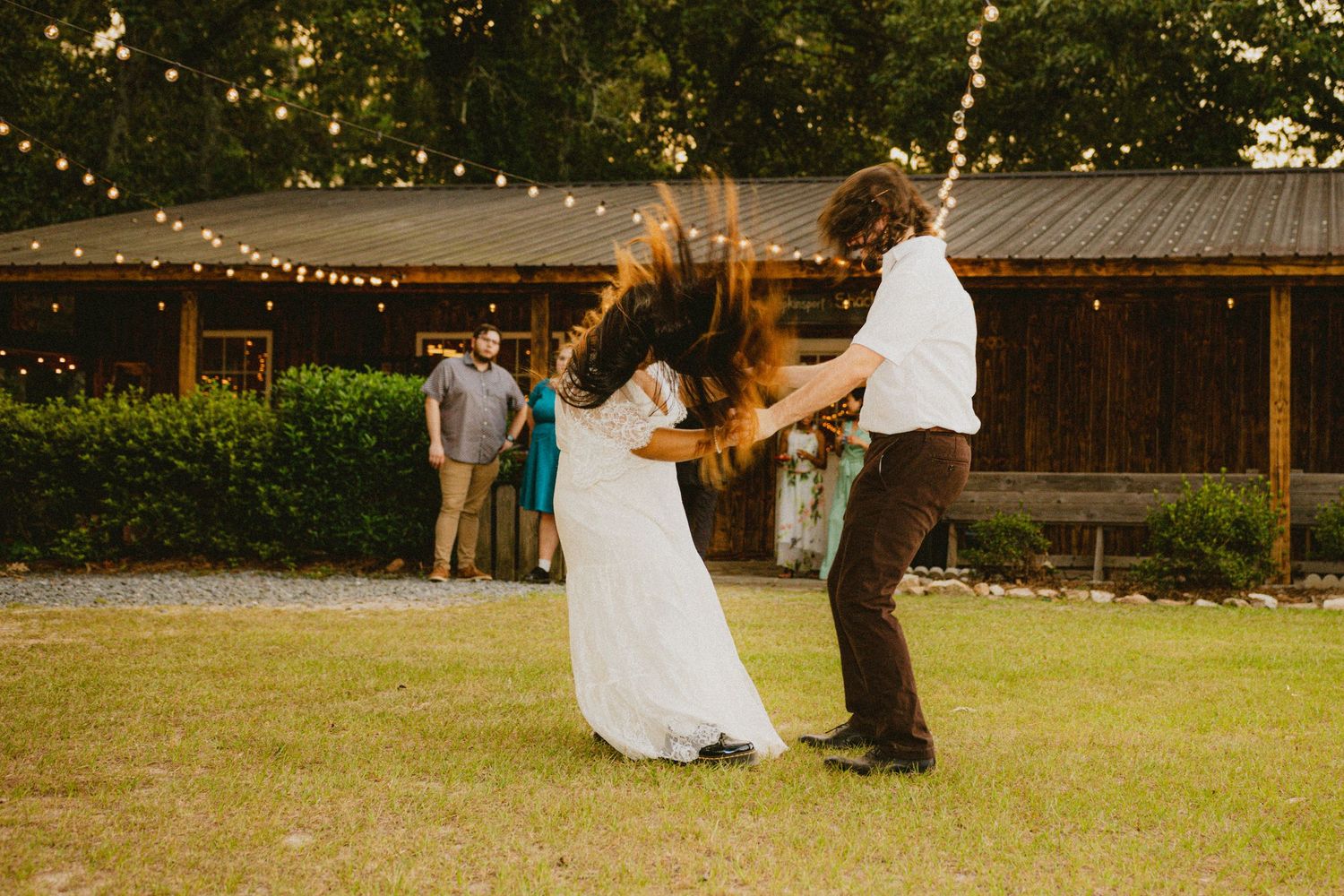 Bride and groom twirling together outdoors at evening wedding reception with string lights.
