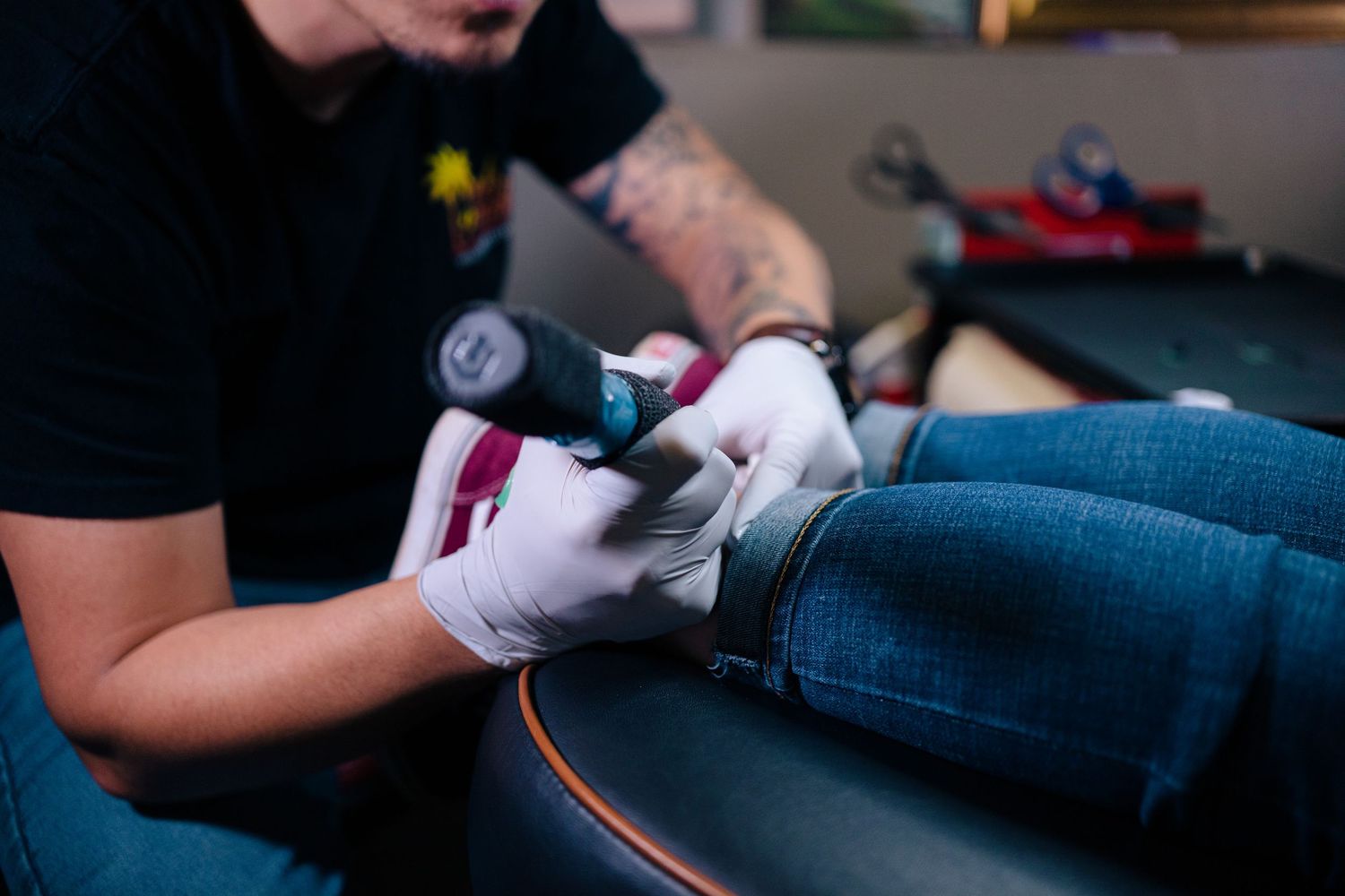 Tattoo artist in gloves applying ink to a client's ankle in a professional tattoo studio.
