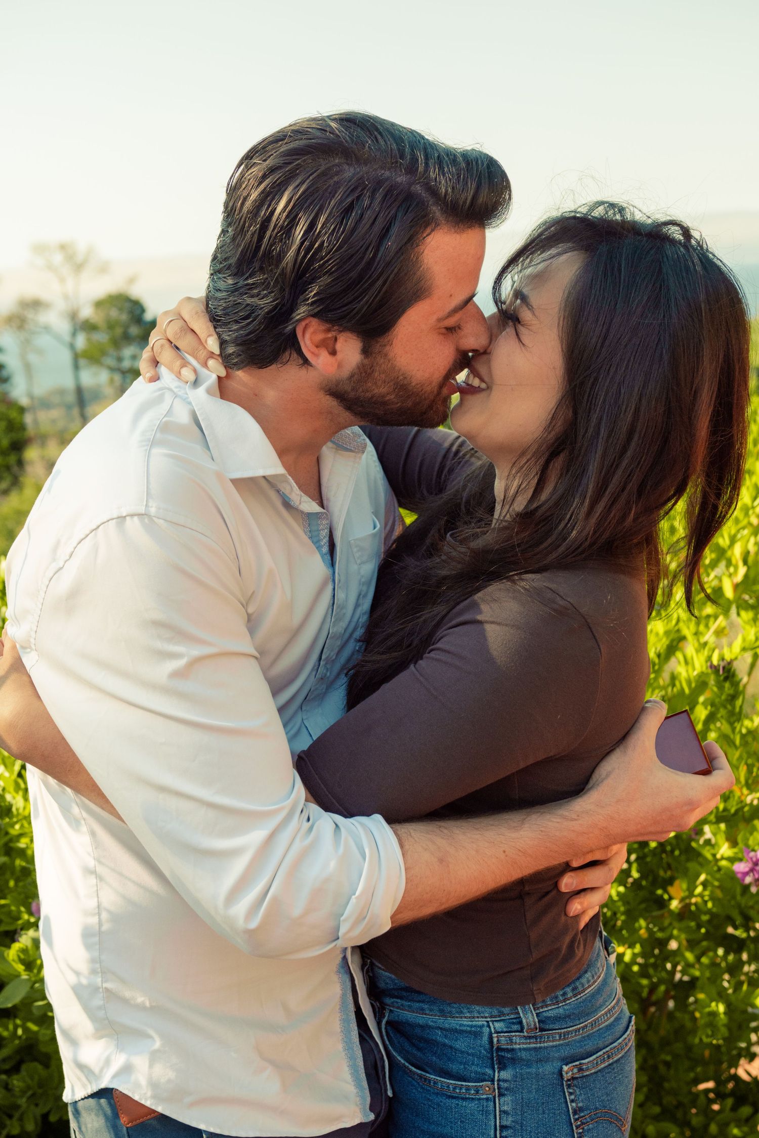 Romantic couple embracing and kissing in a lush green vineyard on a sunny day.