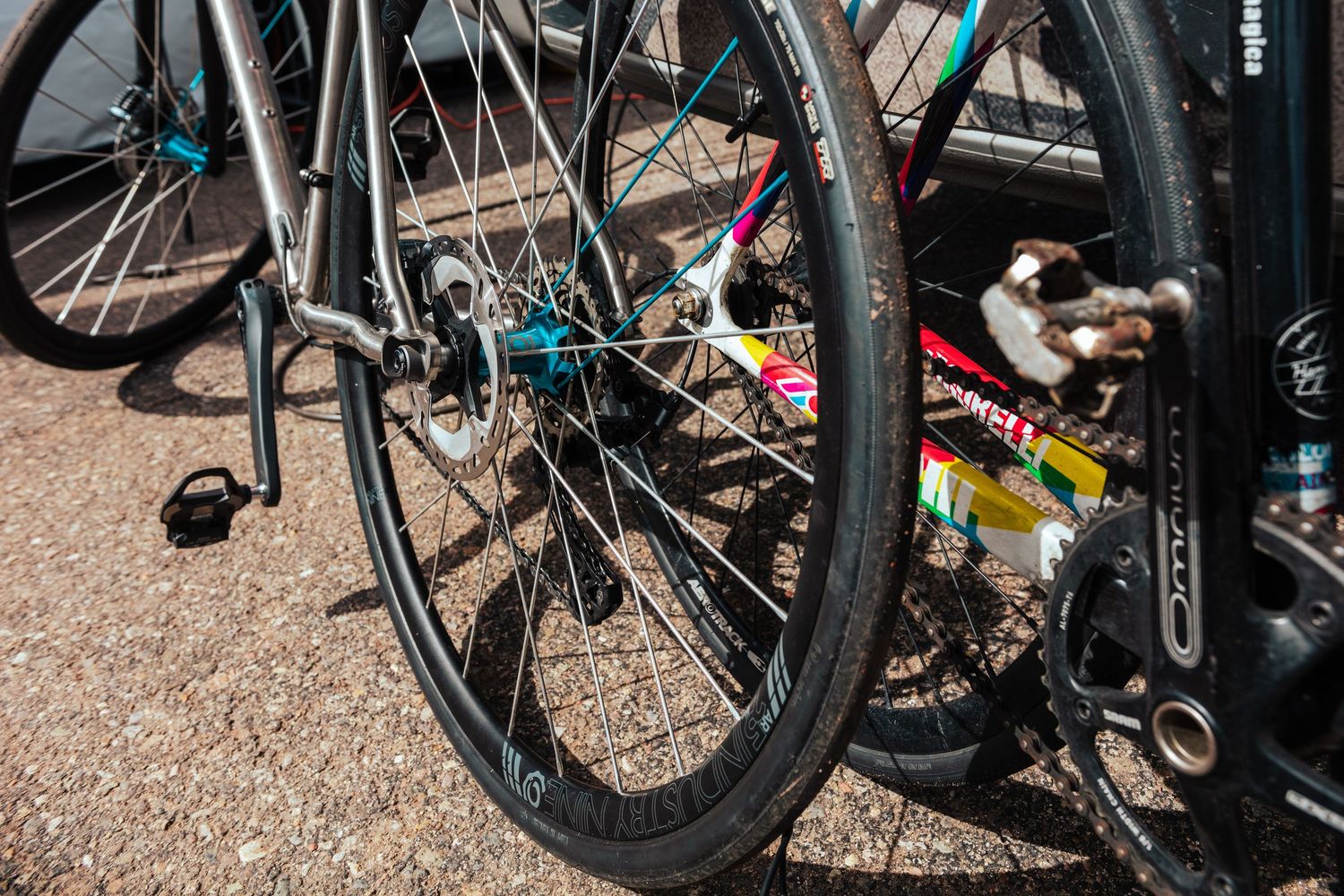Close-up of bicycle wheels with colorful stickers parked on pavement at an outdoor bike event.
