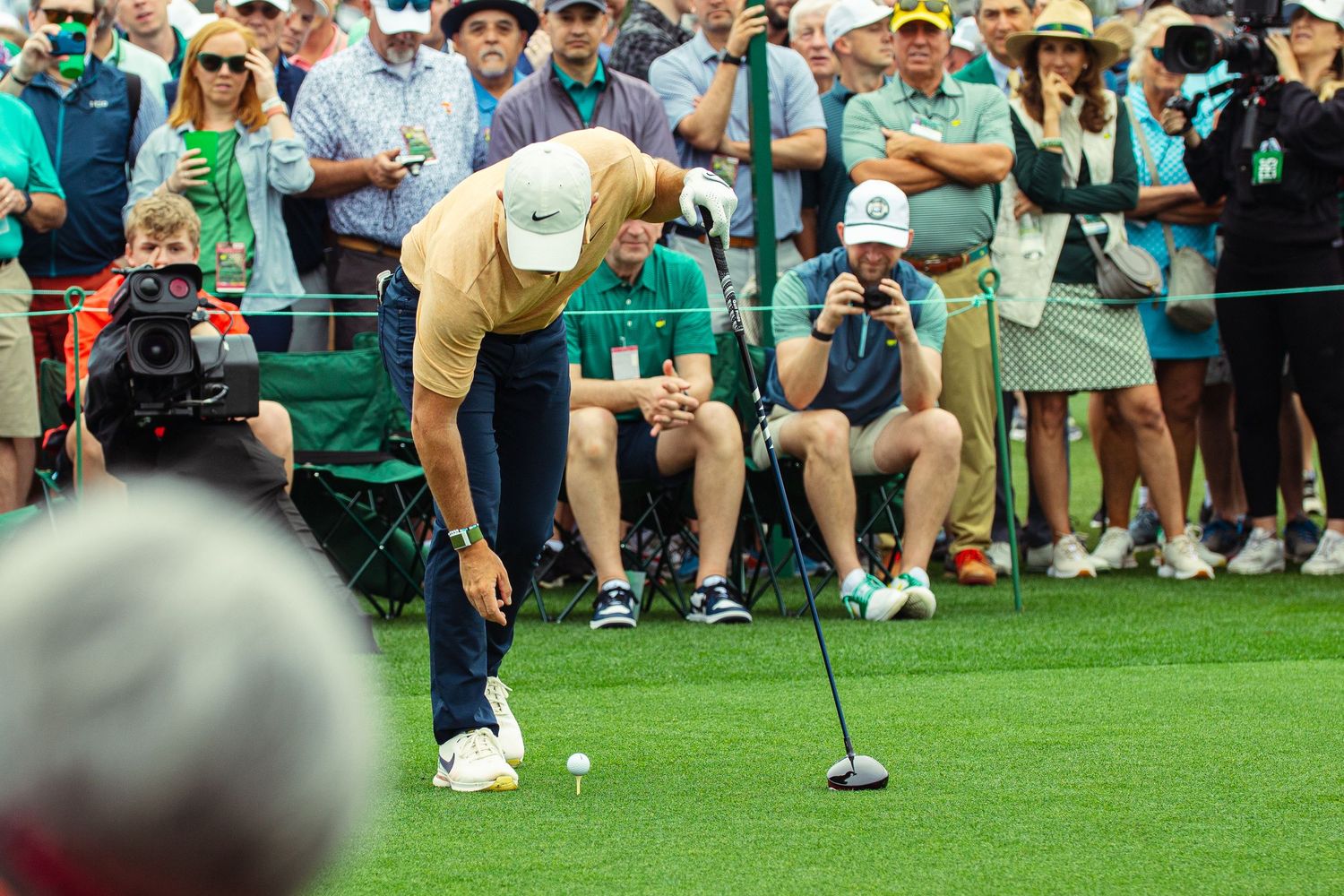 Golfer putting on green at Masters Tournament, surrounded by spectators and photographers.