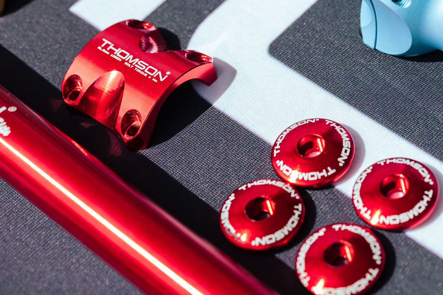 Red anodized Thomson bicycle stem and bolts displayed on a gray surface with branding visible.