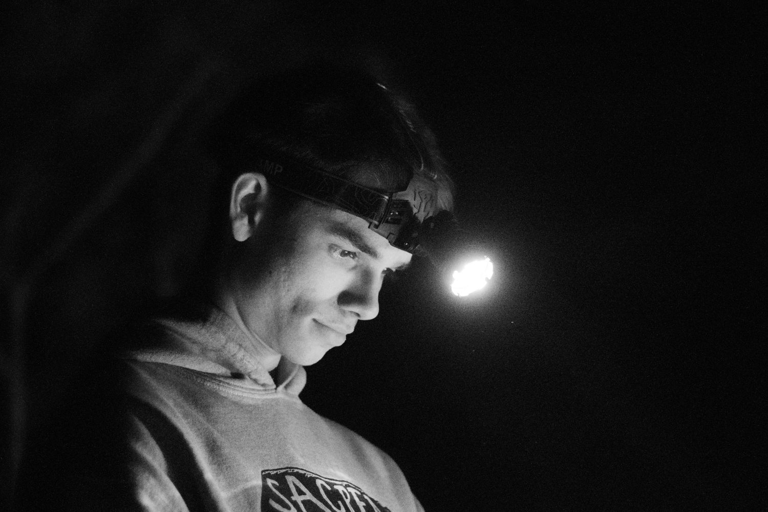 Black and white portrait of a young man wearing a headlamp outdoors at night.