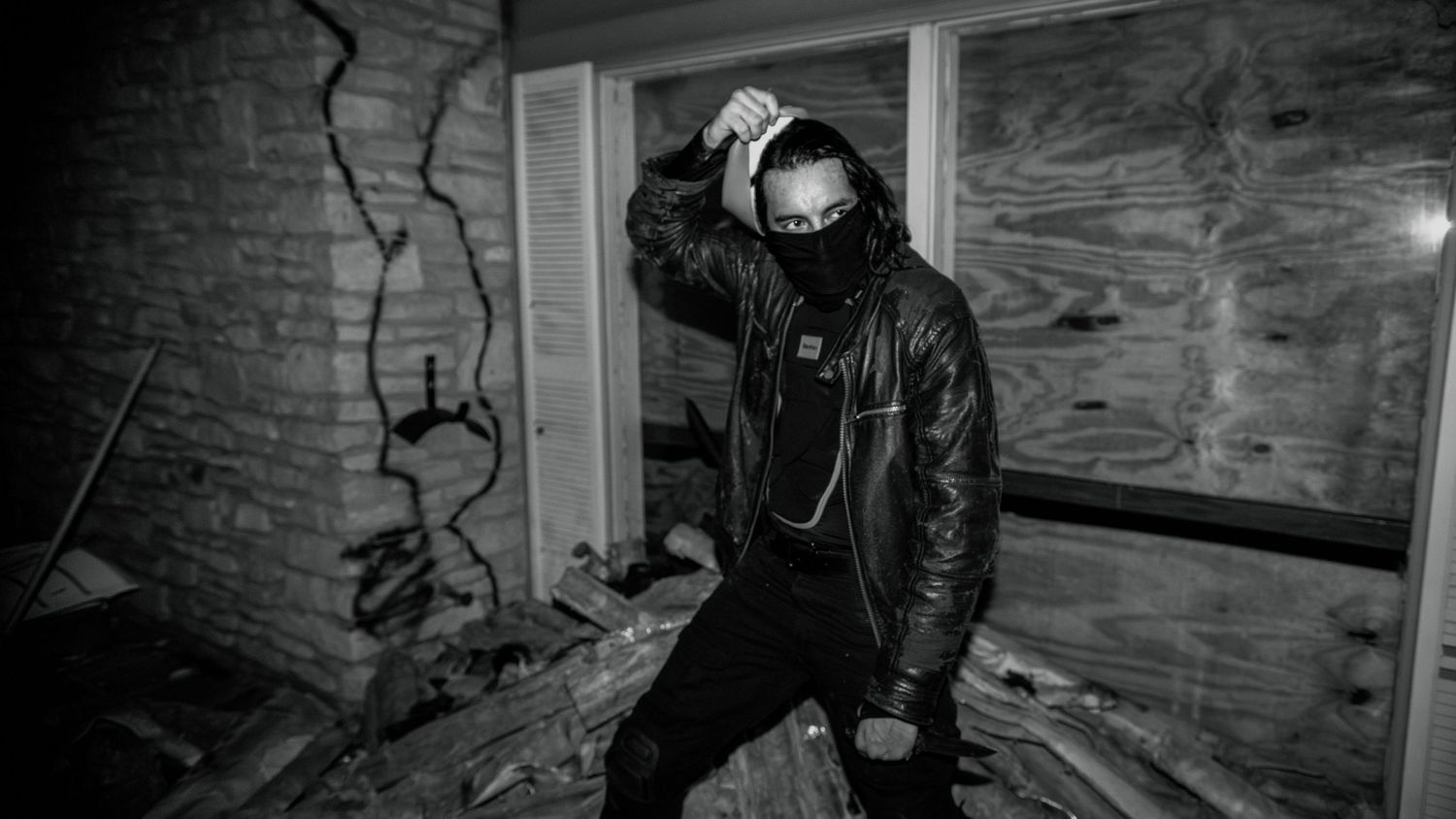 Black and white photo of masked person in leather jacket in abandoned building.
