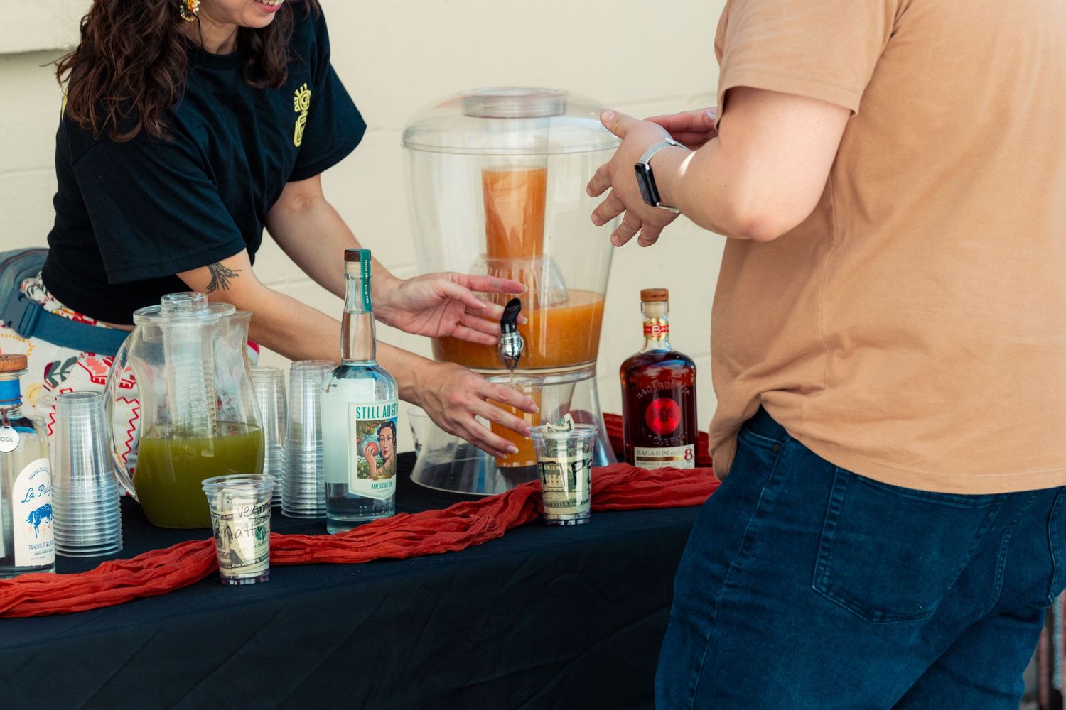 Outdoor drink station with juices, liquor bottles, and glasses being served at a casual event.