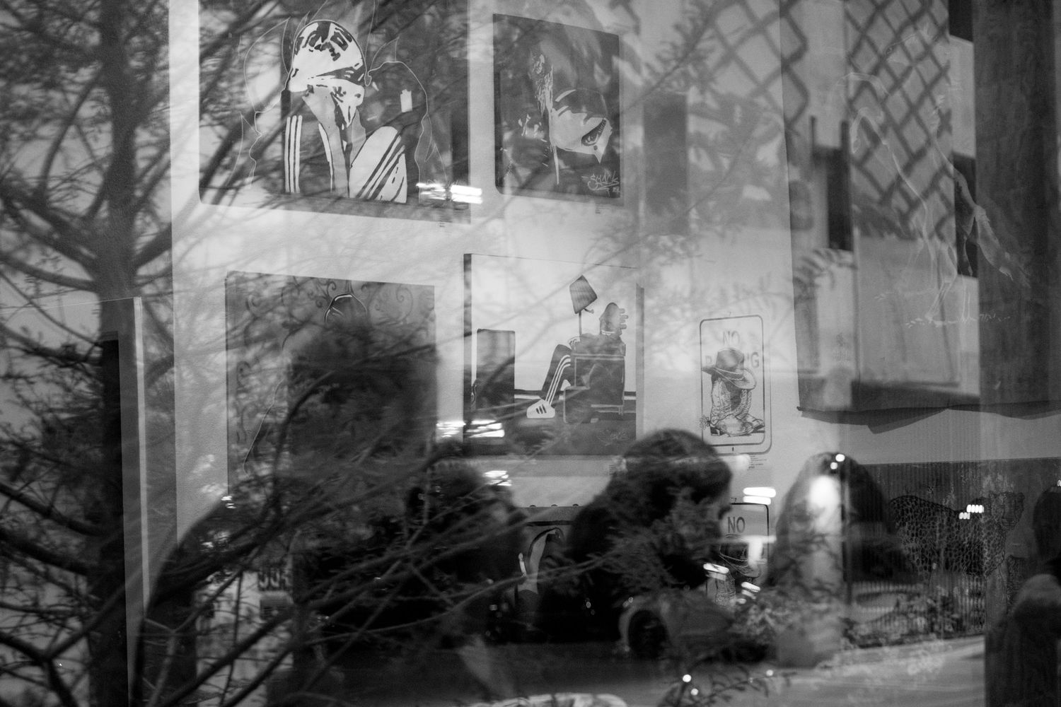Black and white reflection photo of artwork and a person visible through a gallery window at night.