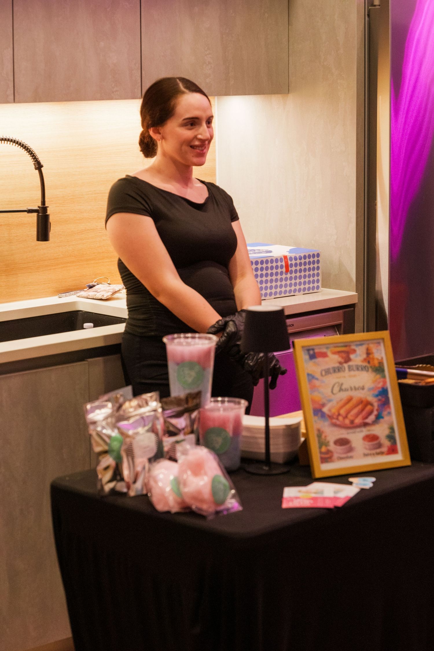 Woman in black dress smiling behind a dessert table with cotton candy and cherry blossom themed treats at an event.