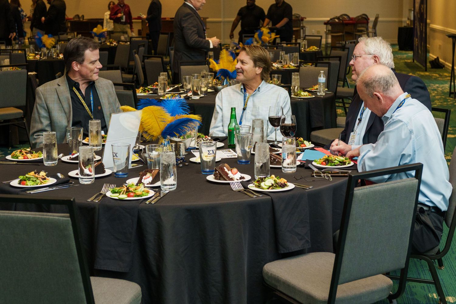 Three men enjoying a formal dinner at a round table in a banquet hall, with wine glasses and salads.