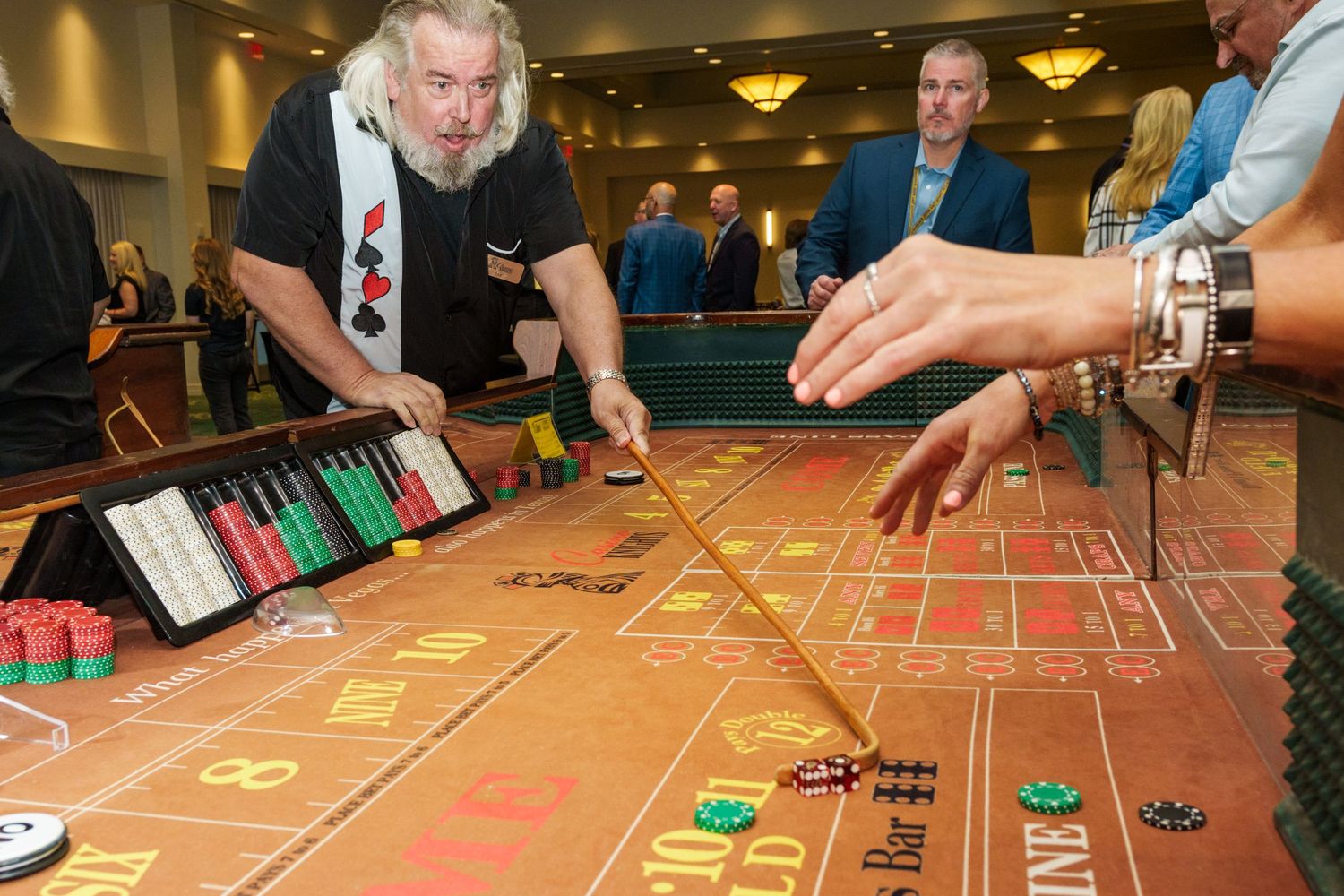 Man dealing craps at a casino table with colorful chips and dice during a lively gambling event.