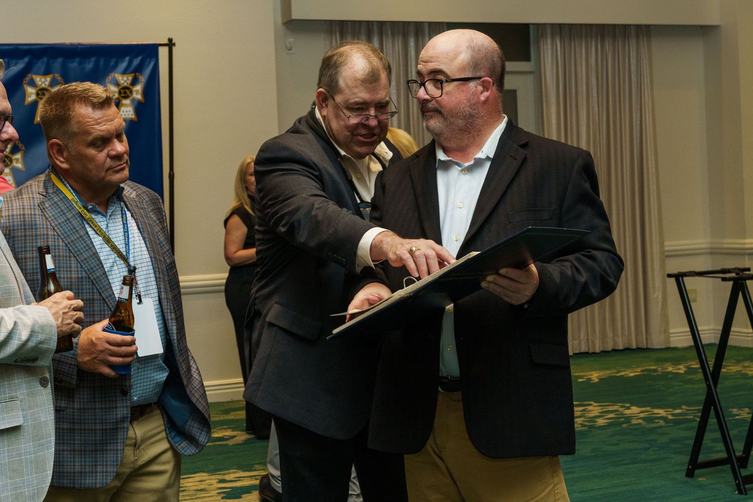 Two men in business casual attire review a document together at an indoor professional event or awards ceremony.