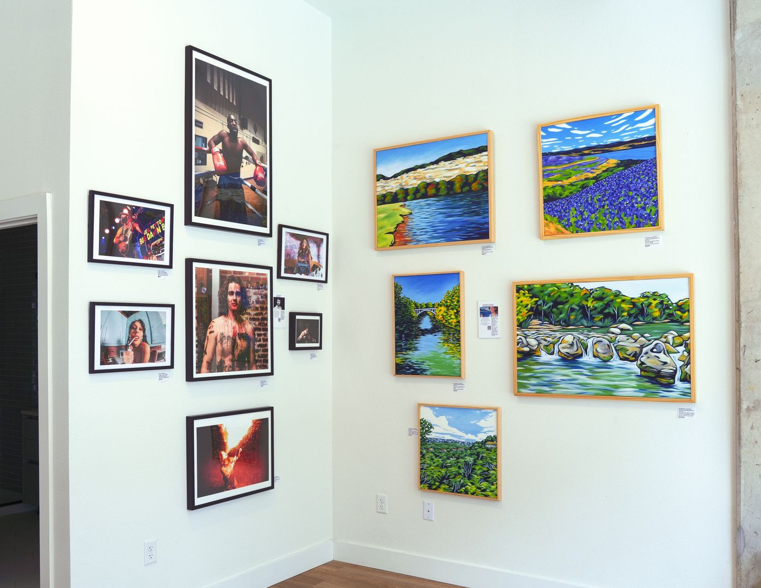 Art gallery wall displaying colorful landscape paintings and framed photography prints in a bright white corner space.