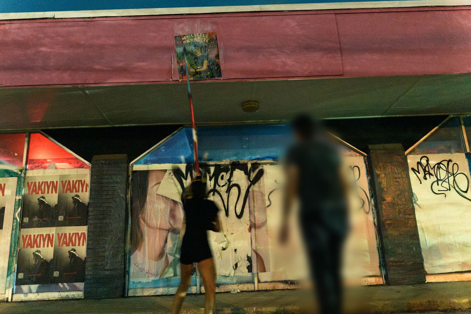 People standing near a graffiti-covered building at night with posters on the walls.