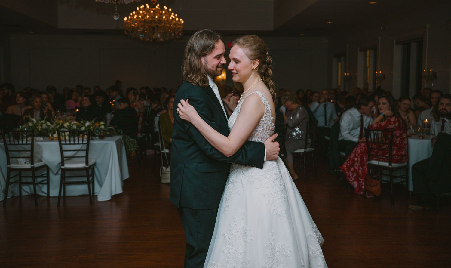 Bride and groom sharing their first dance in an elegant ballroom reception venue with chandelier lighting.