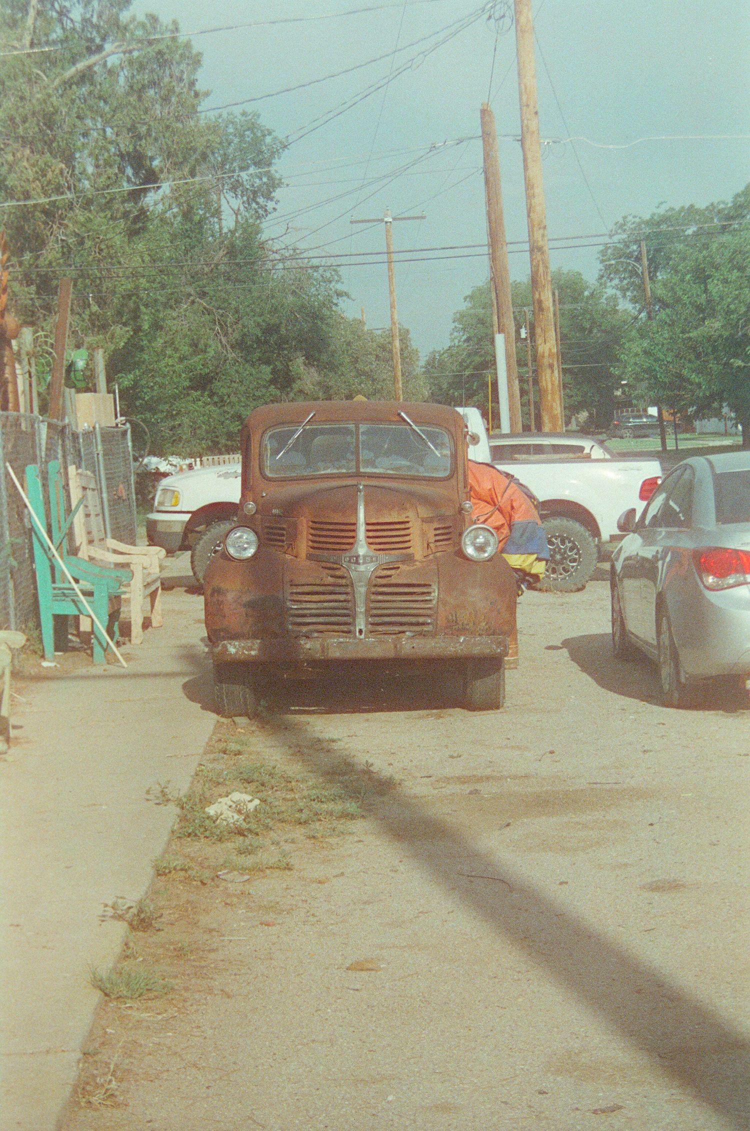Rusty vintage Dodge truck parked on a street beside modern cars and utility poles.