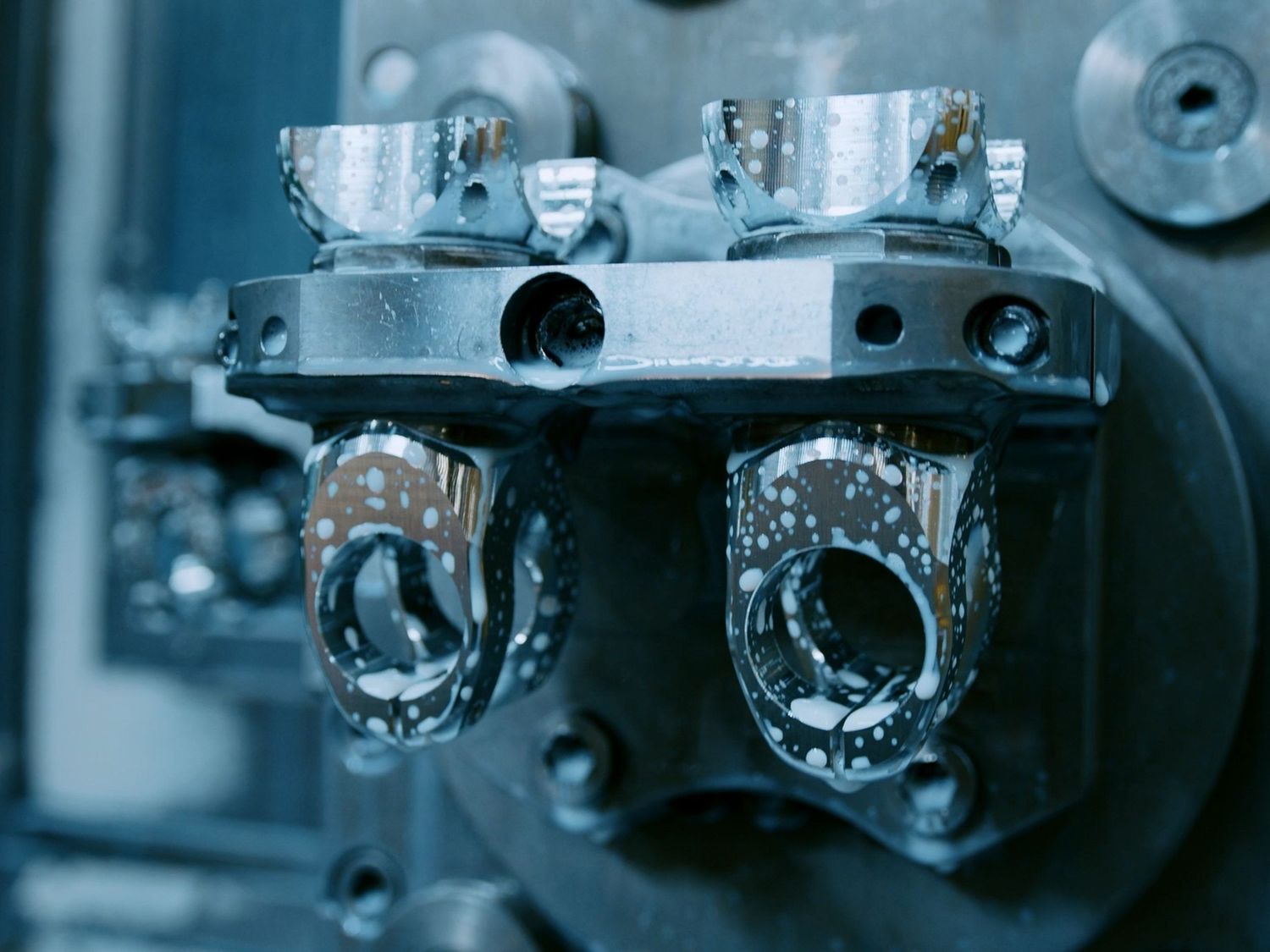 Close-up of machined metal engine components with polished cylindrical bores in blue tint.