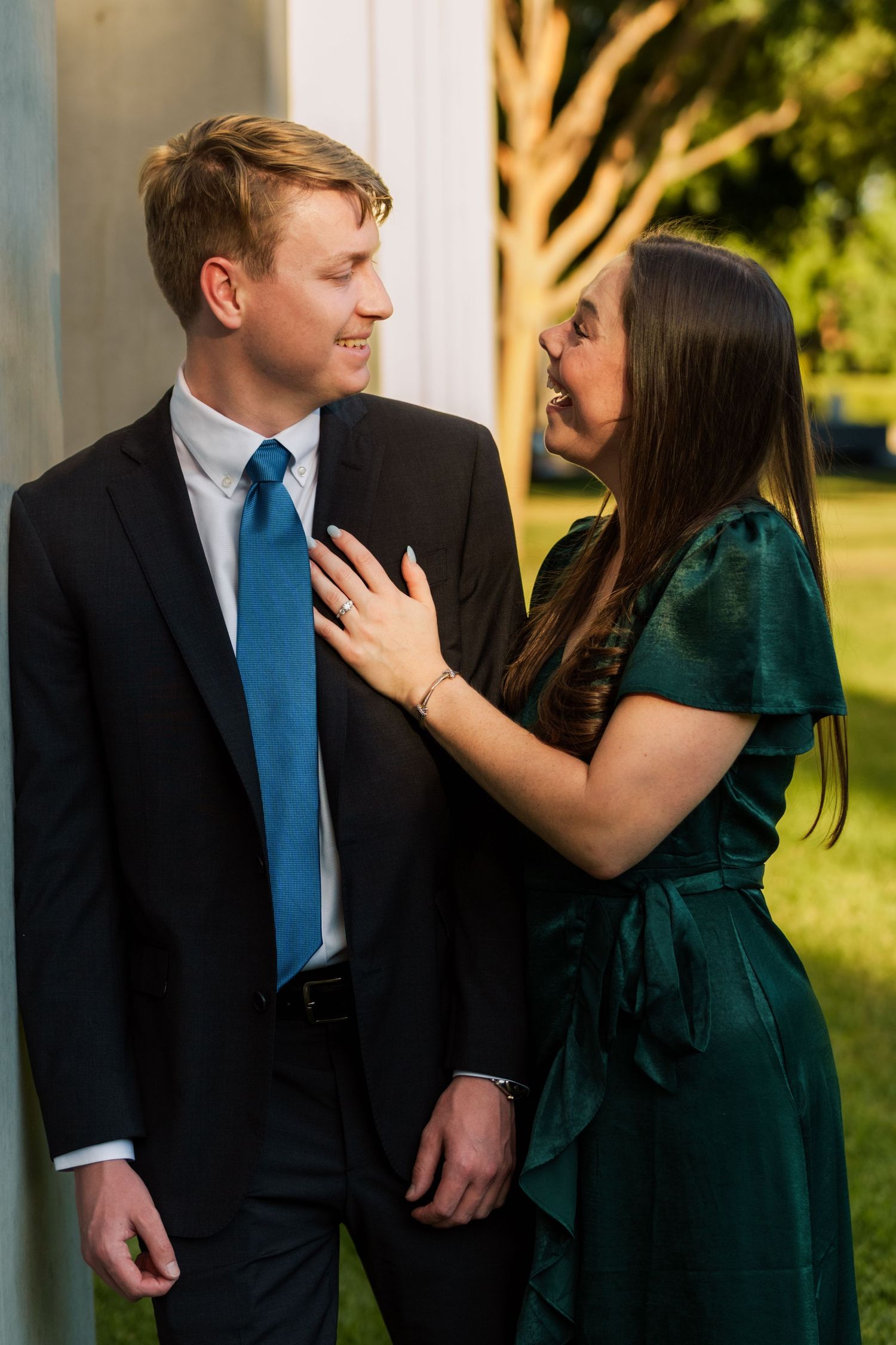 Couple in formal wear smiling at each other, man in black suit with blue tie, woman in green velvet dress.