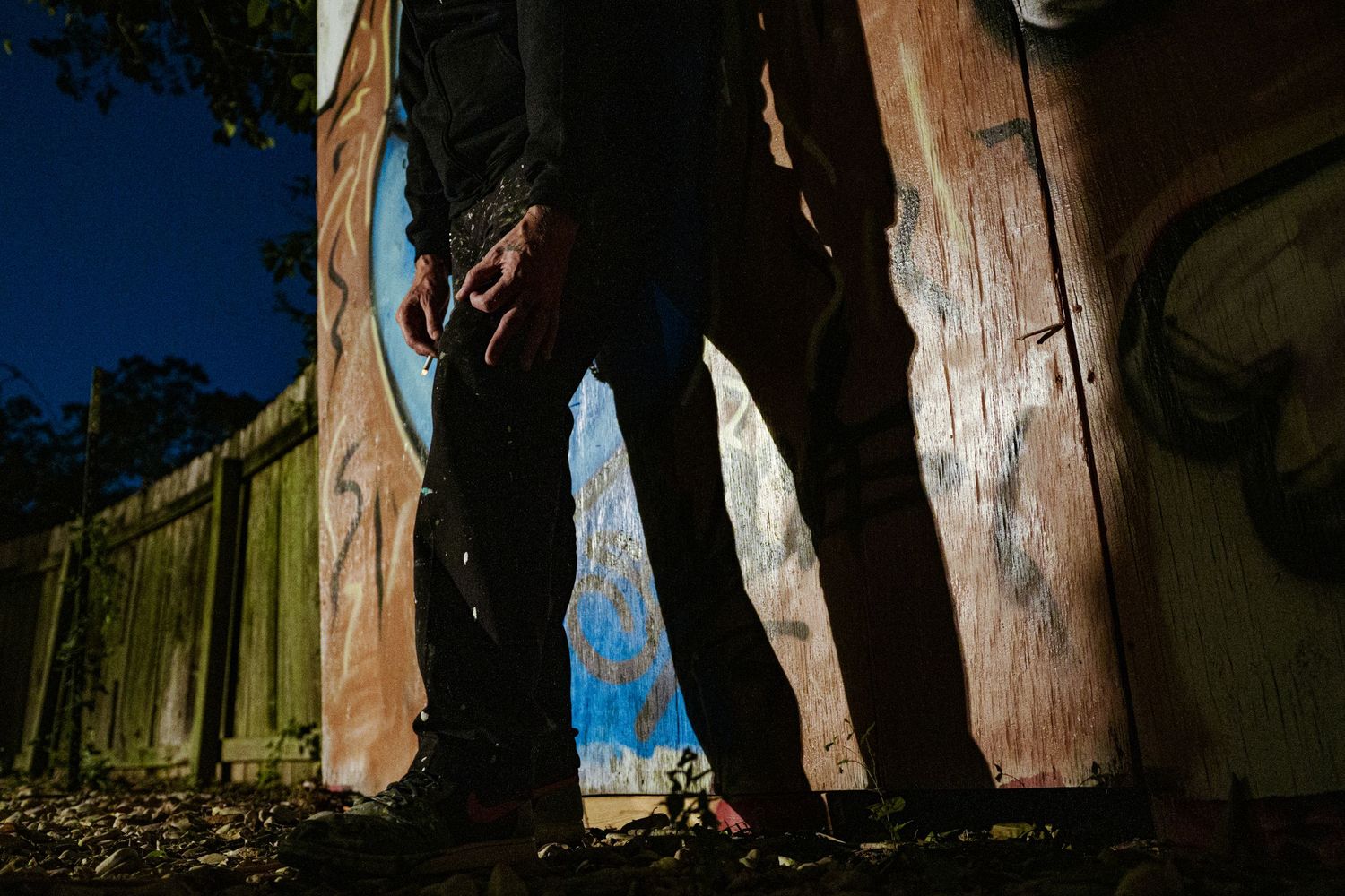 Low angle view of a person standing between weathered wooden boards in dramatic outdoor lighting.