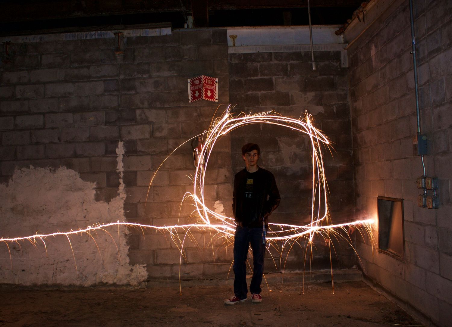 Person standing in front of a brick wall with glowing light painting circle created by sparklers at night.