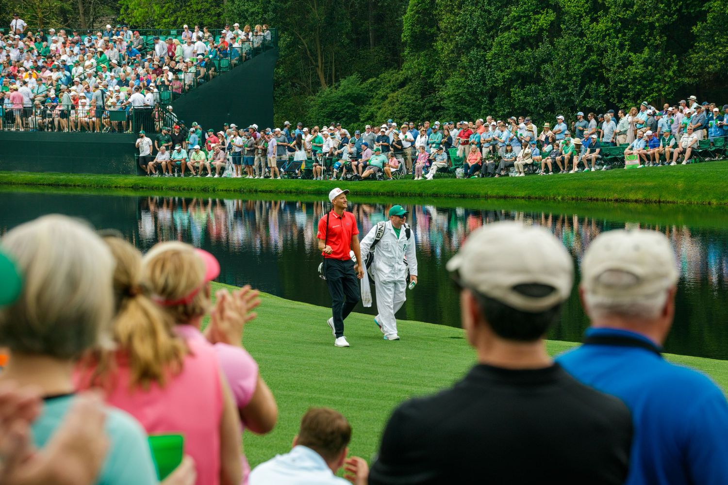 Golfer and caddie walk fairway at Augusta National during The Masters, watched by large gallery of spectators.