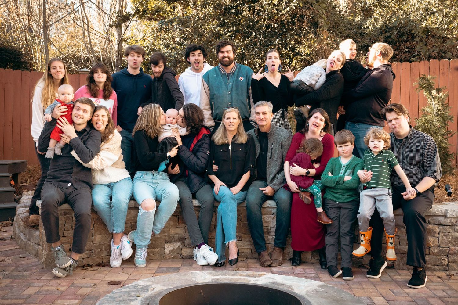 Extended family group portrait laughing outdoors in a cozy backyard setting in winter.