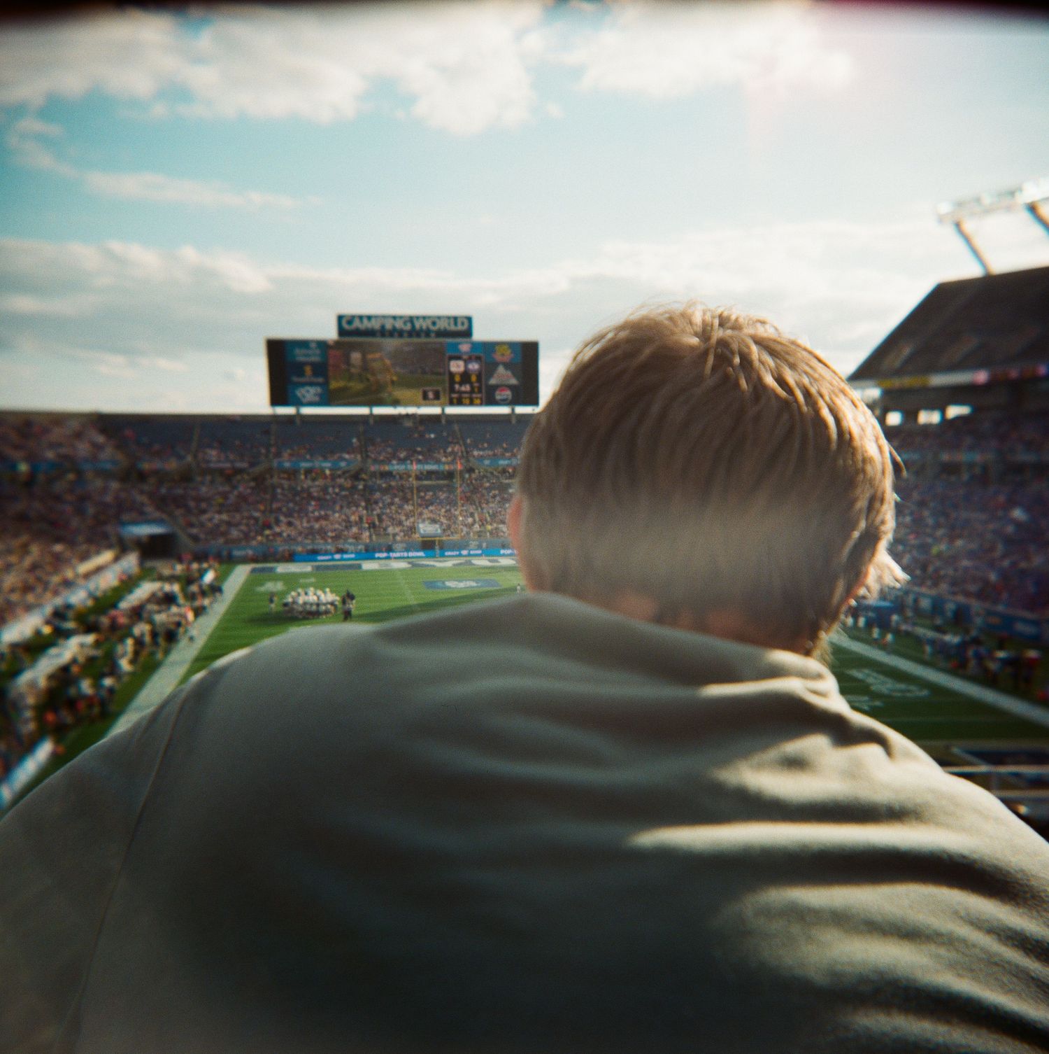 Back of mans head overlooking packed Camping World Stadium during sunny college football game.