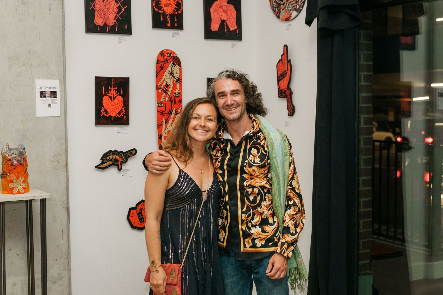 Smiling couple posing together in front of red and black artwork at art gallery.