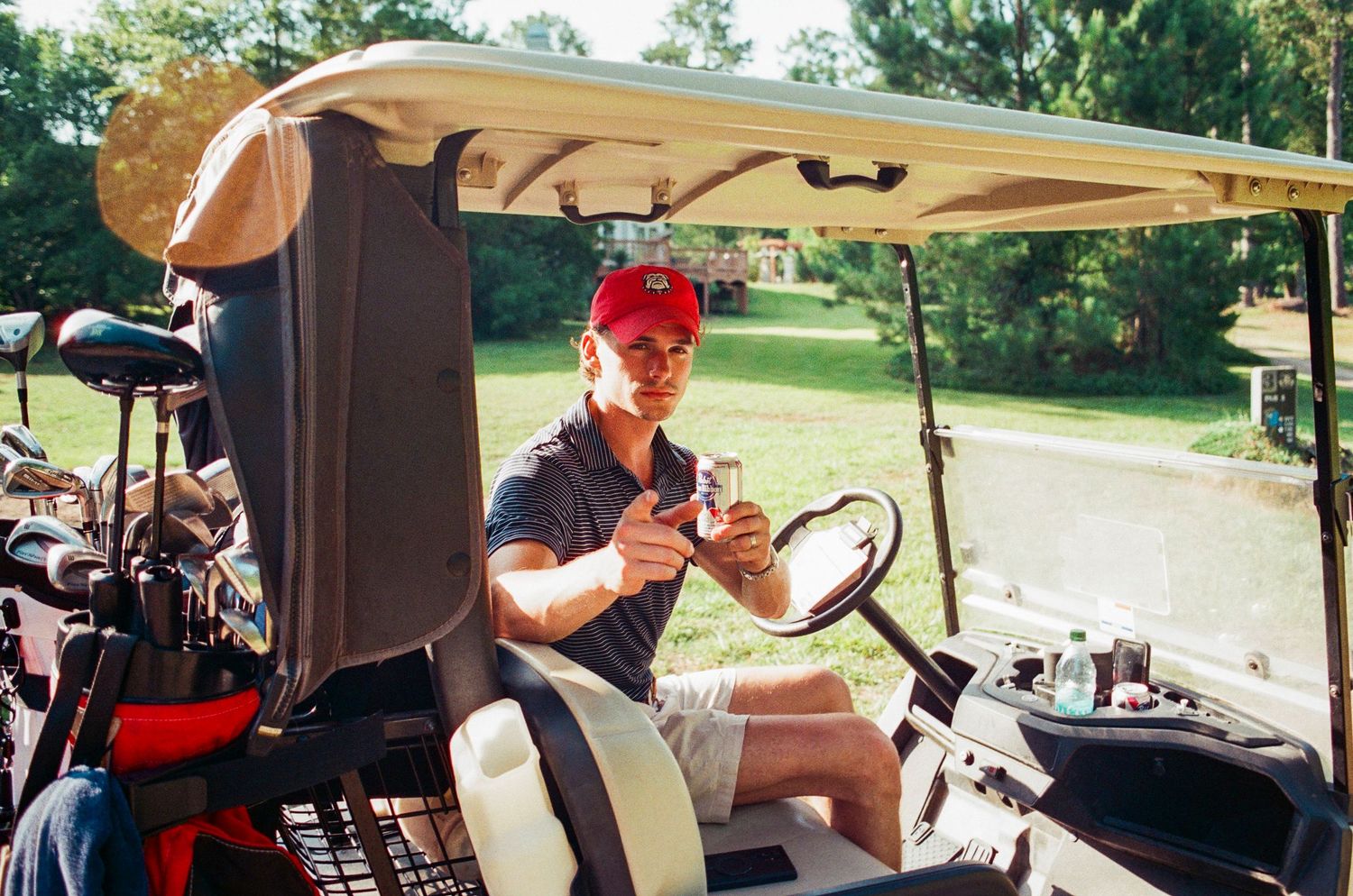 Man sitting in a golf cart reviewing scorecard at a tree-lined golf course on a sunny day.