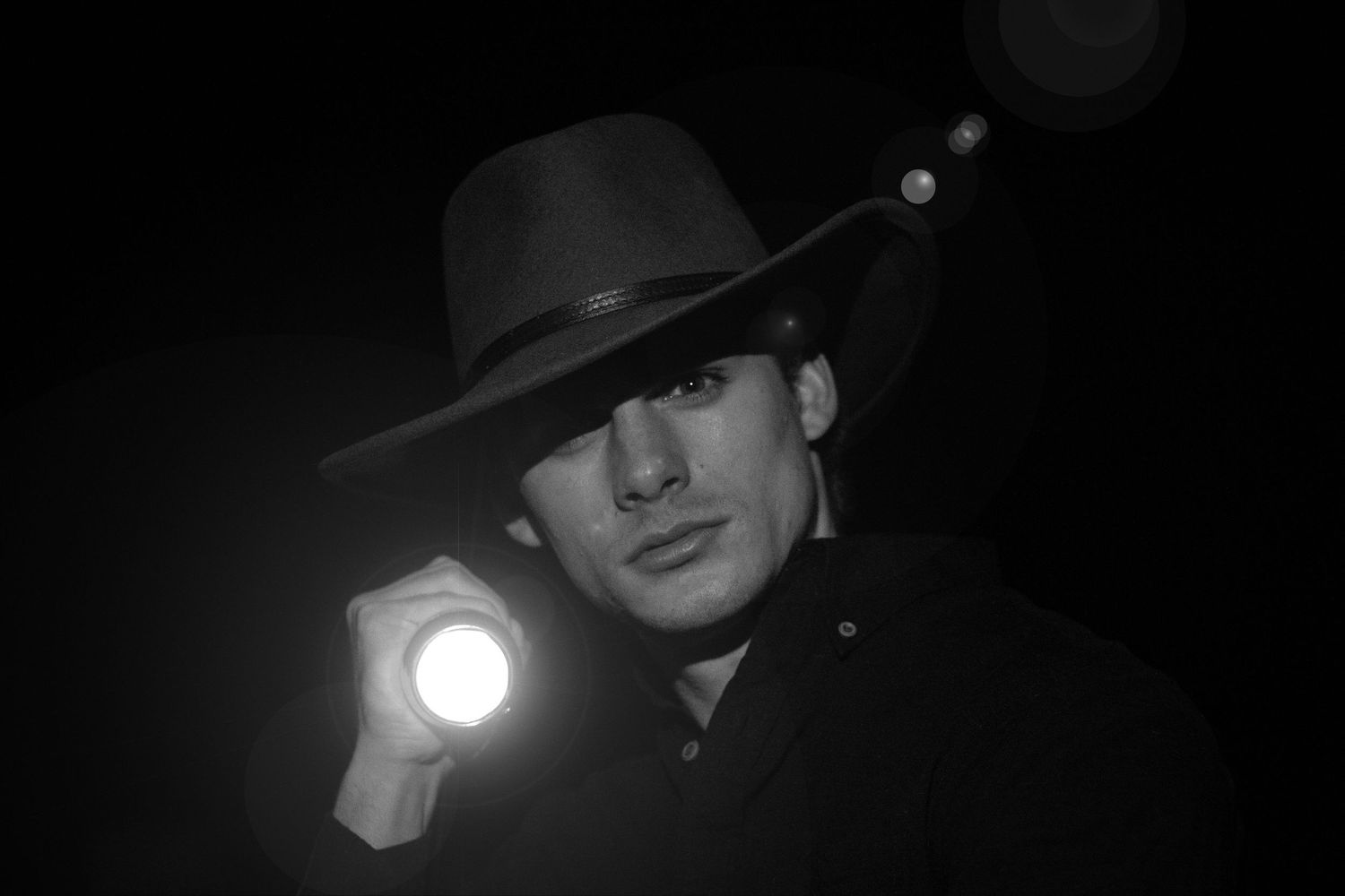 Black and white photo of a man in a cowboy hat holding a flashlight in the dark.
