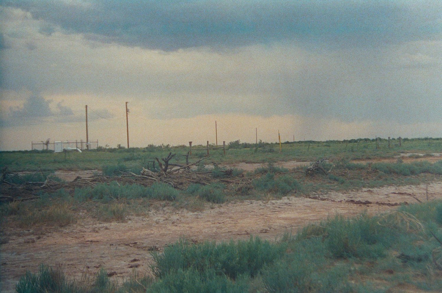 Vast flat grassland under stormy skies with utility poles stretching across the horizon on a rural dirt road.