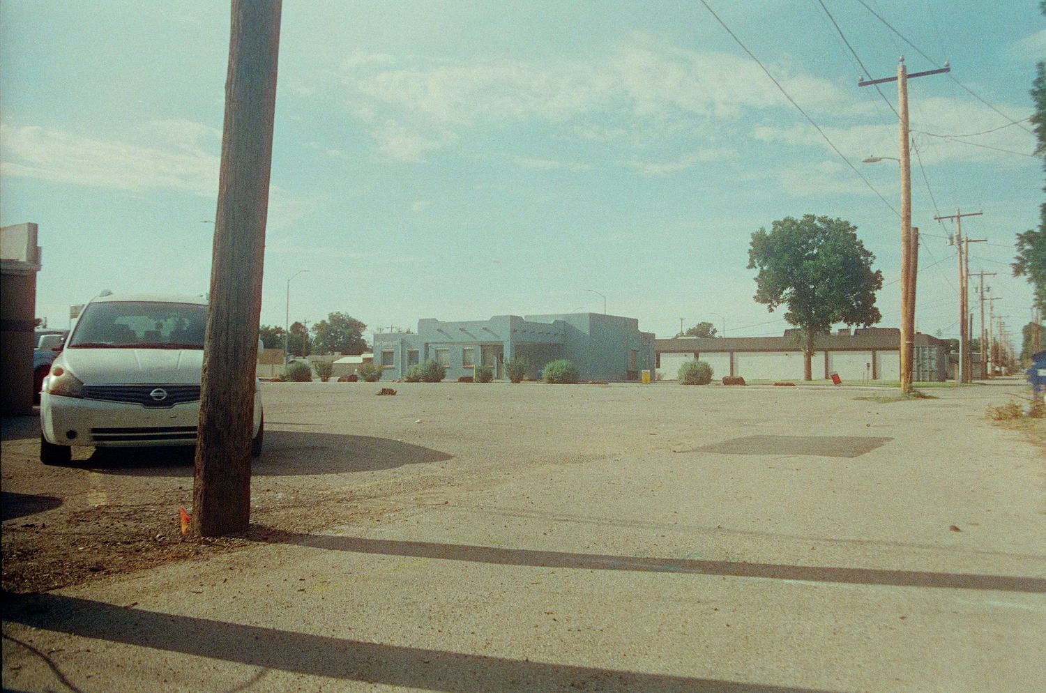 A minivan parked near a utility pole in a sparse desert town parking lot with commercial buildings in the background.