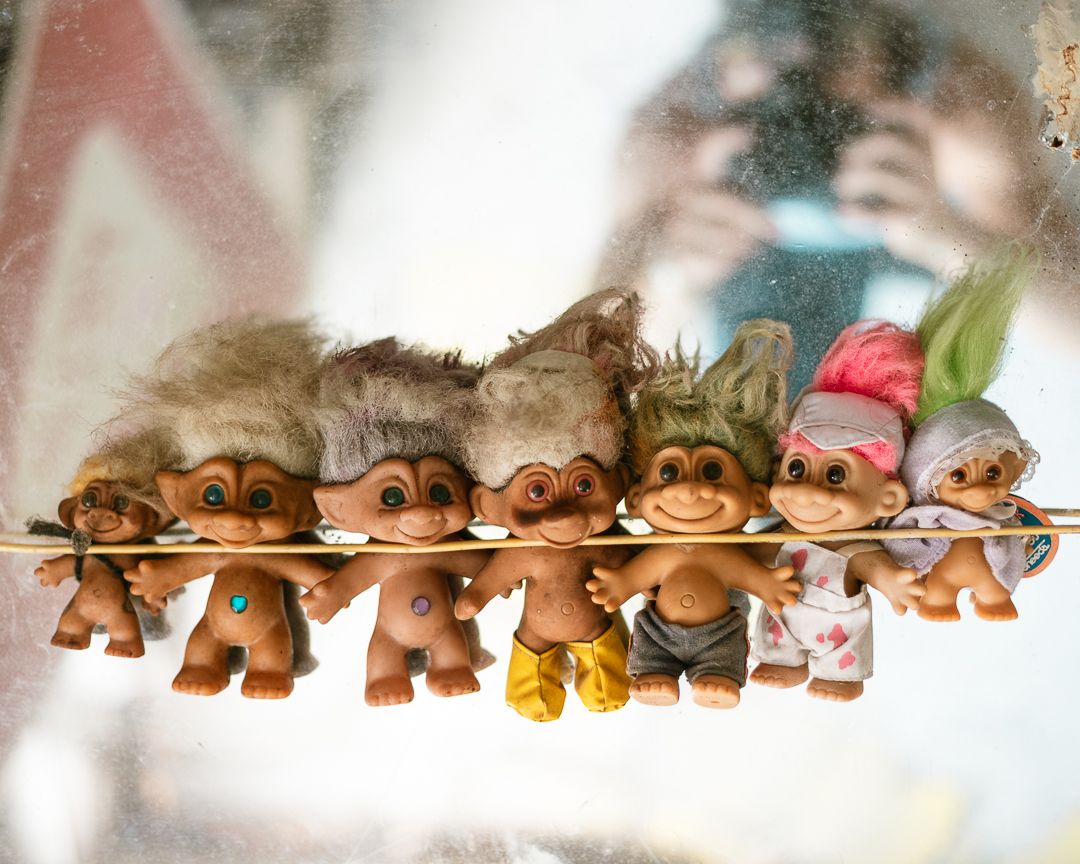 Collection of vintage troll dolls with colorful hair displayed on a rod, reflecting in a mirror.