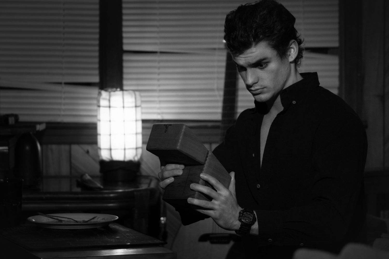 Young man in dark shirt examining a box under lamp light in black and white photo.