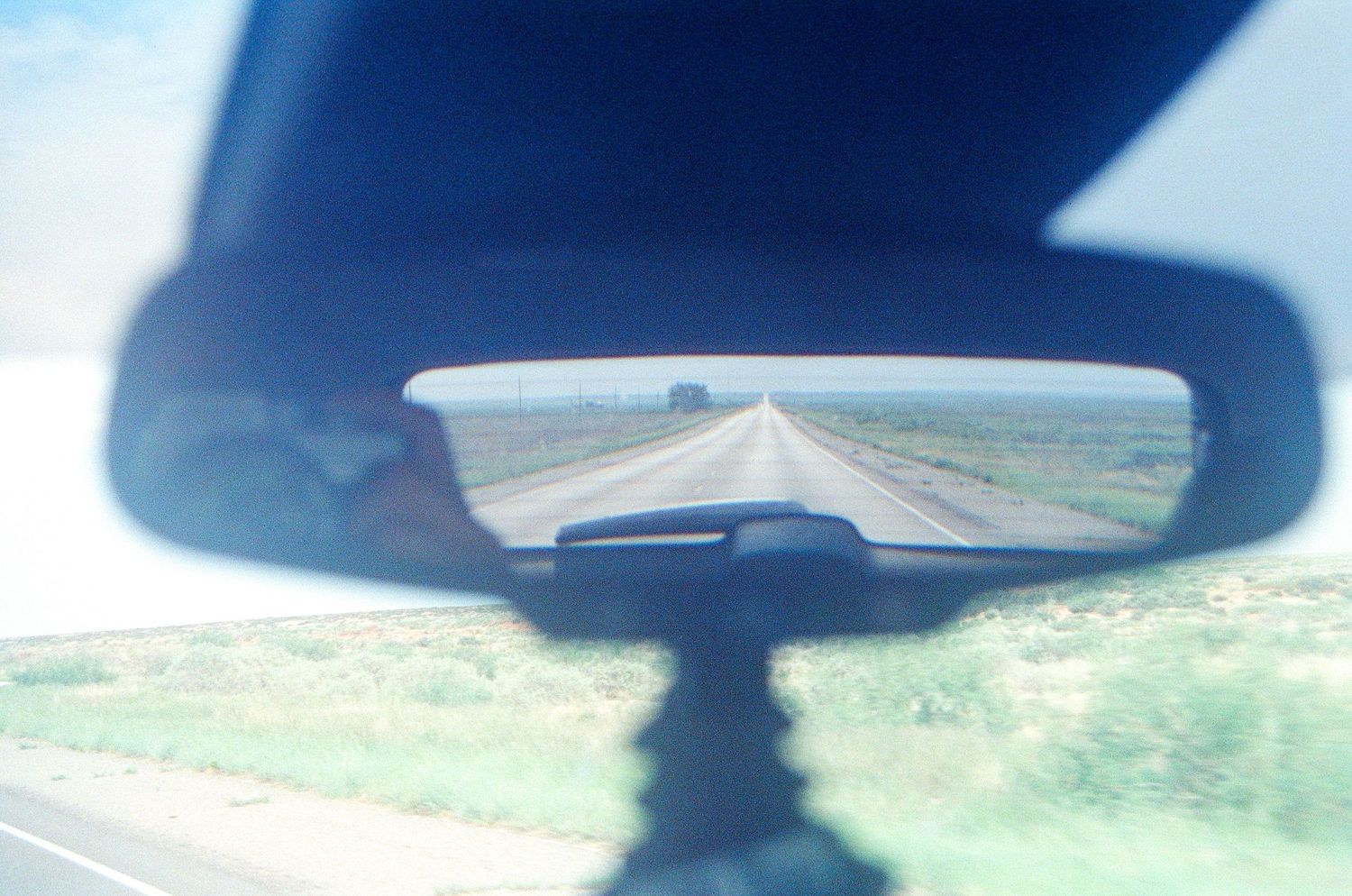 Rear view mirror reflection showing an open highway stretching into the distance through a rural landscape.