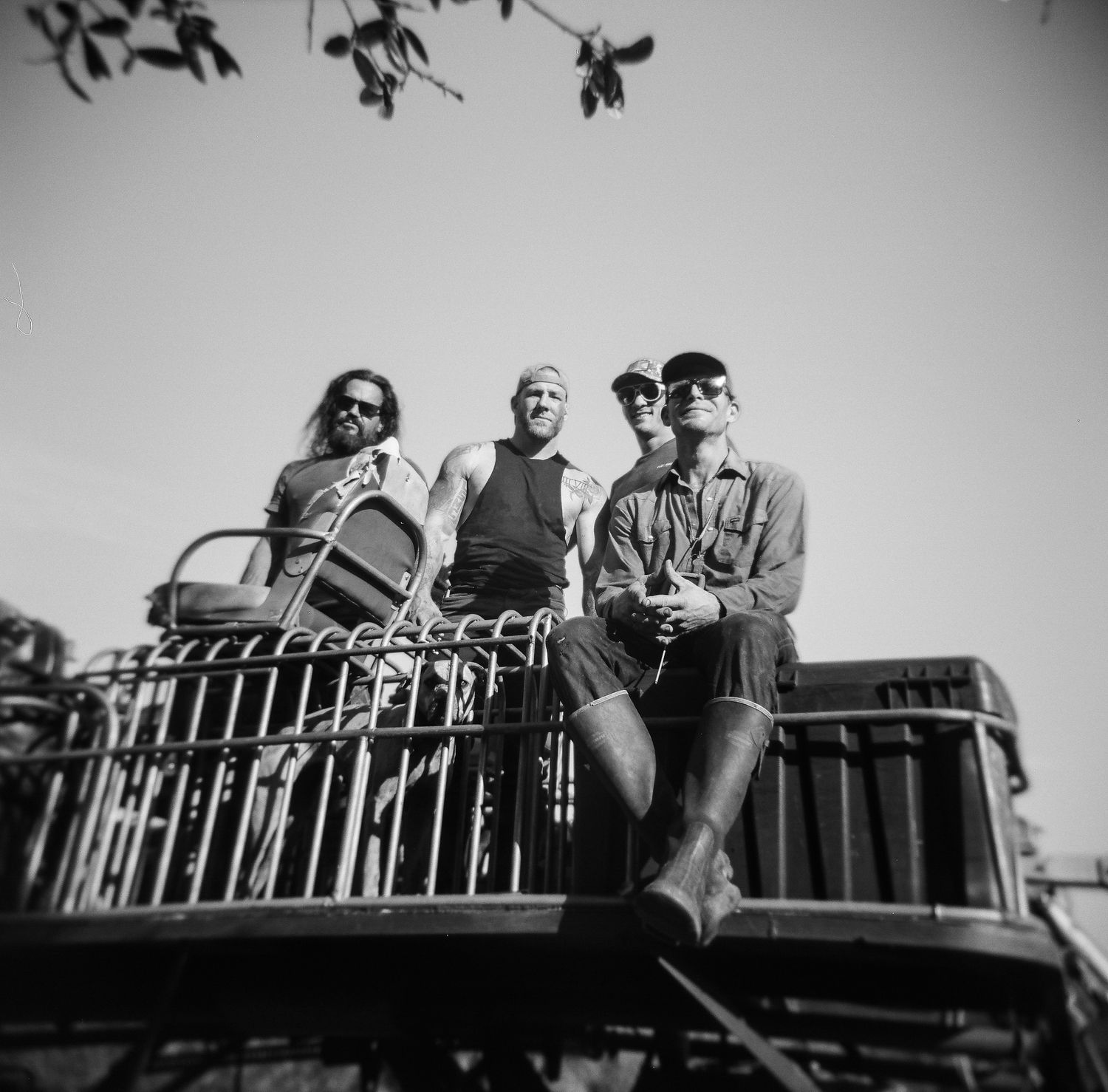 Three men sitting on top of a vintage vehicle outdoors in a black and white photo.